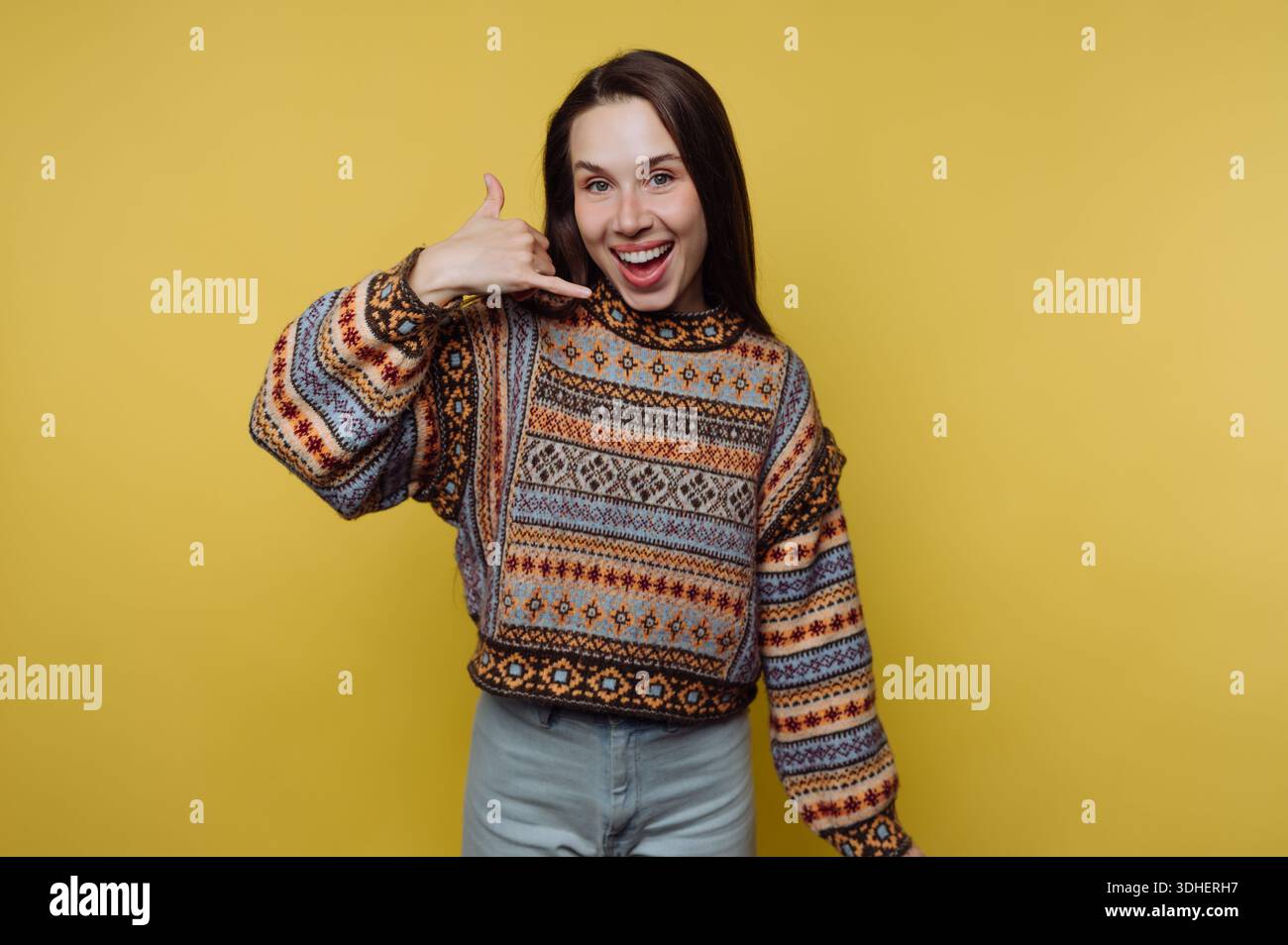 Smiling woman in a patterned sweater making a call me gesture. Stock Photo