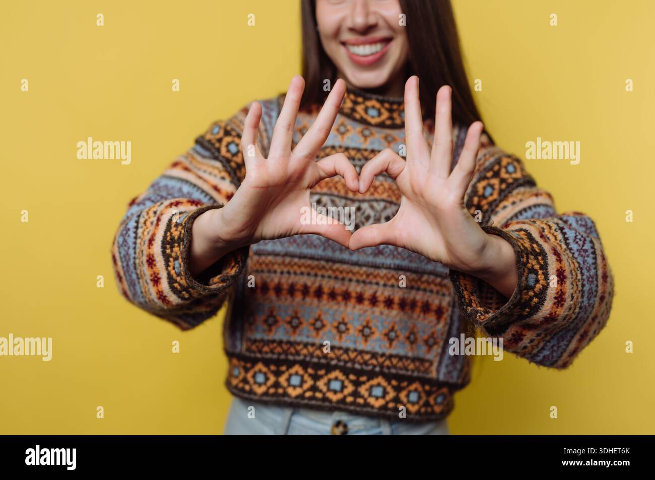 Woman in patterned sweater making heart shape with hands Stock Photo