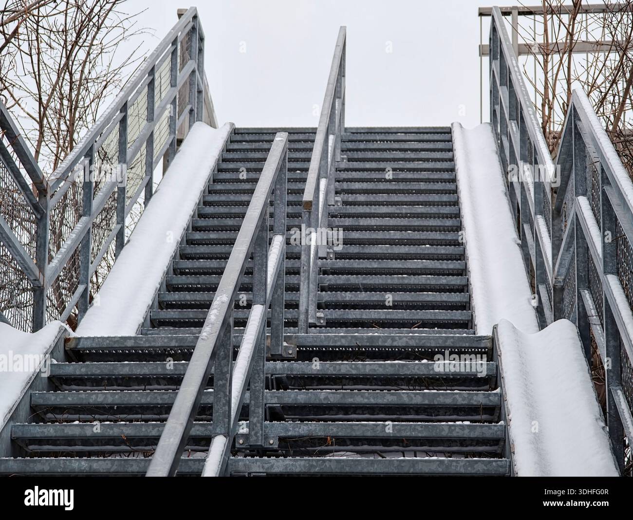 Snow-covered wide steel outdoor staircase with bicycle ramps on both ...