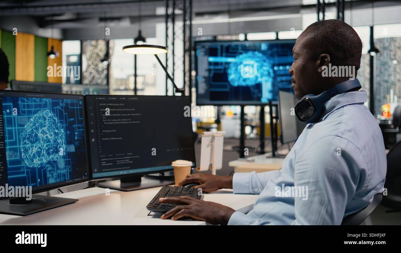 Data scientist in office doing software development to launch new features. African American man in startup company writing computer programs, doing code testing and quality assurance, camera A Stock Photo