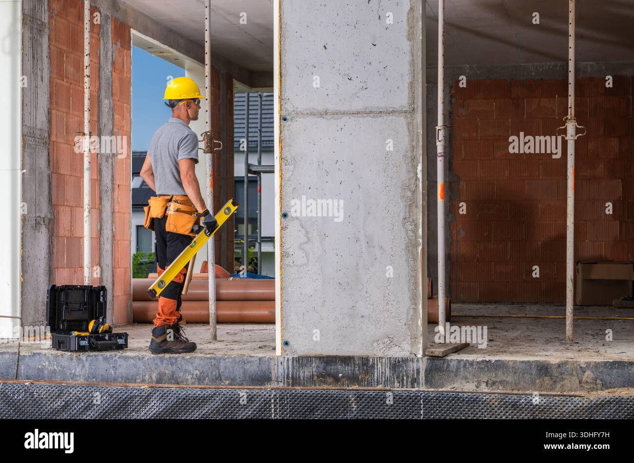 A construction worker stands at a site using a level tool on a wall. Stock Photo