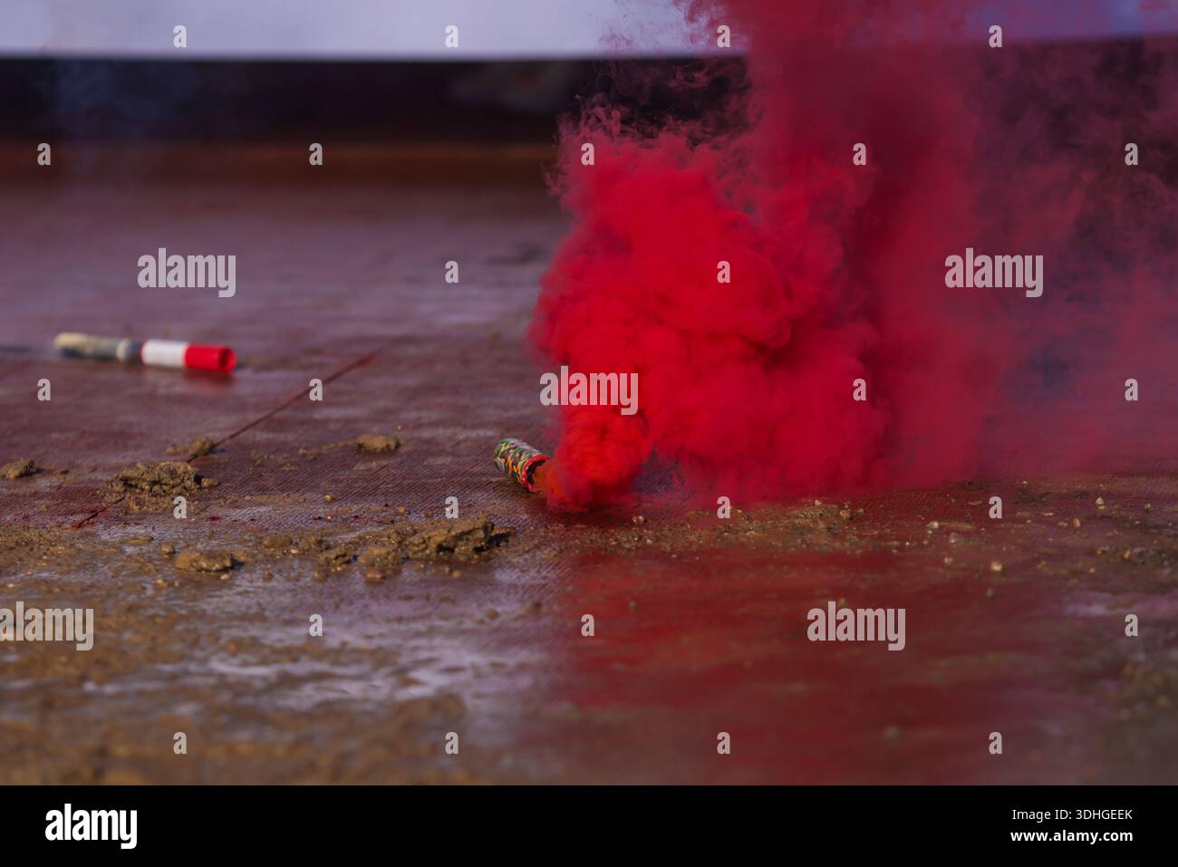Details with a red smoke flare thrown on the ground, in mud. Stock Photo