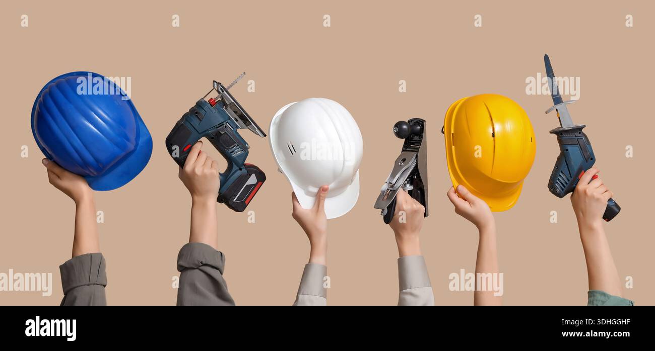 Hands with hardhats and construction tools on beige background Stock Photo