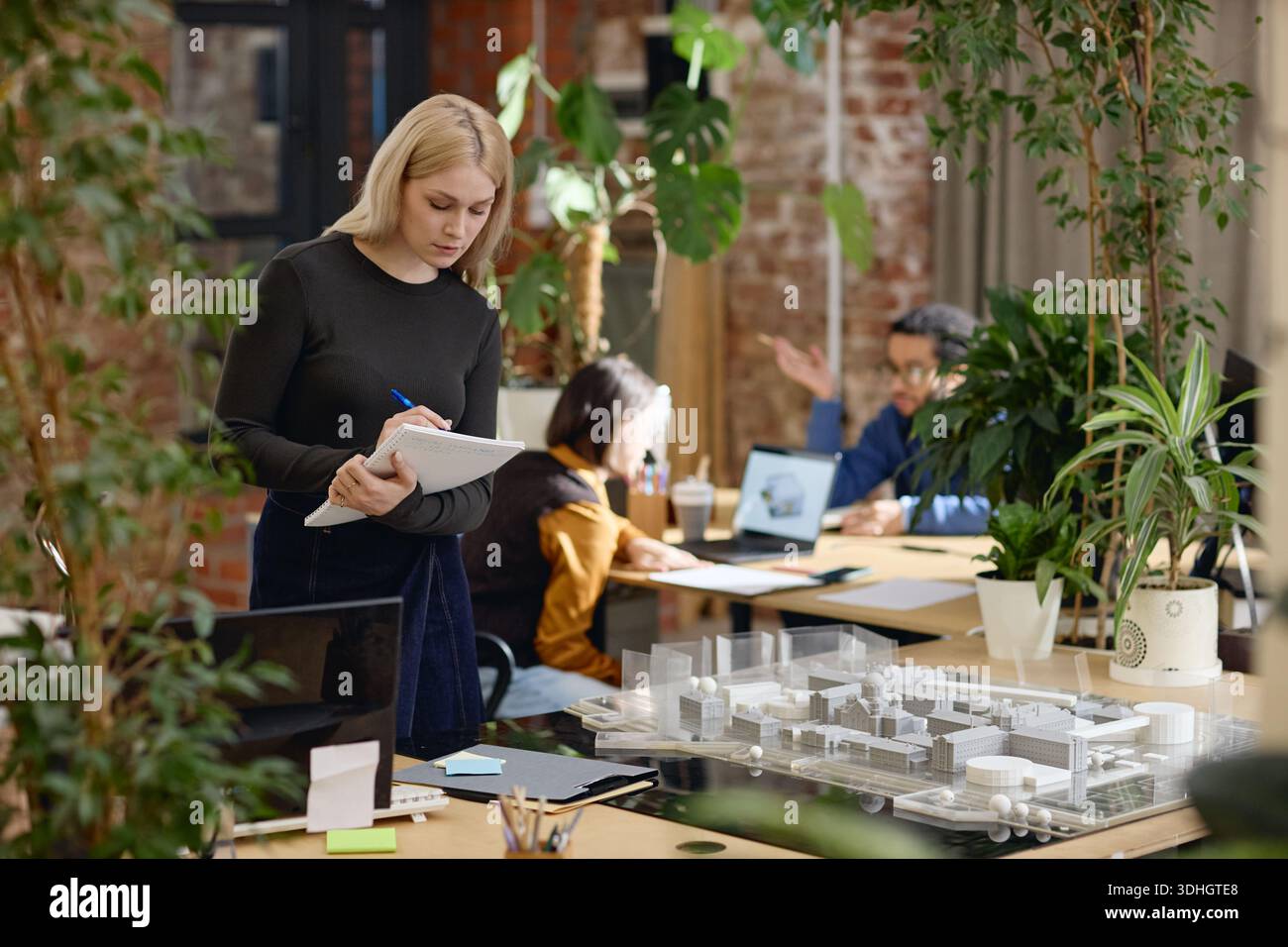 Young Female Architect Writing Notes While Working in Modern Office Workspace Stock Photo