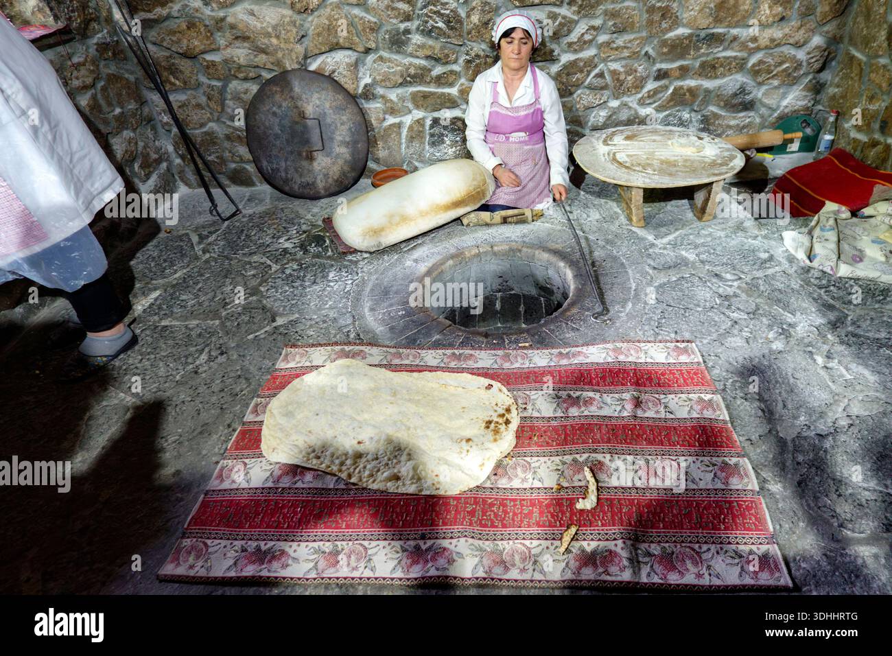 Woman prepares Armenian lavash flatbread in a tonir (traditional underground stone oven) in Armenia, Eastern Europe Stock Photo
