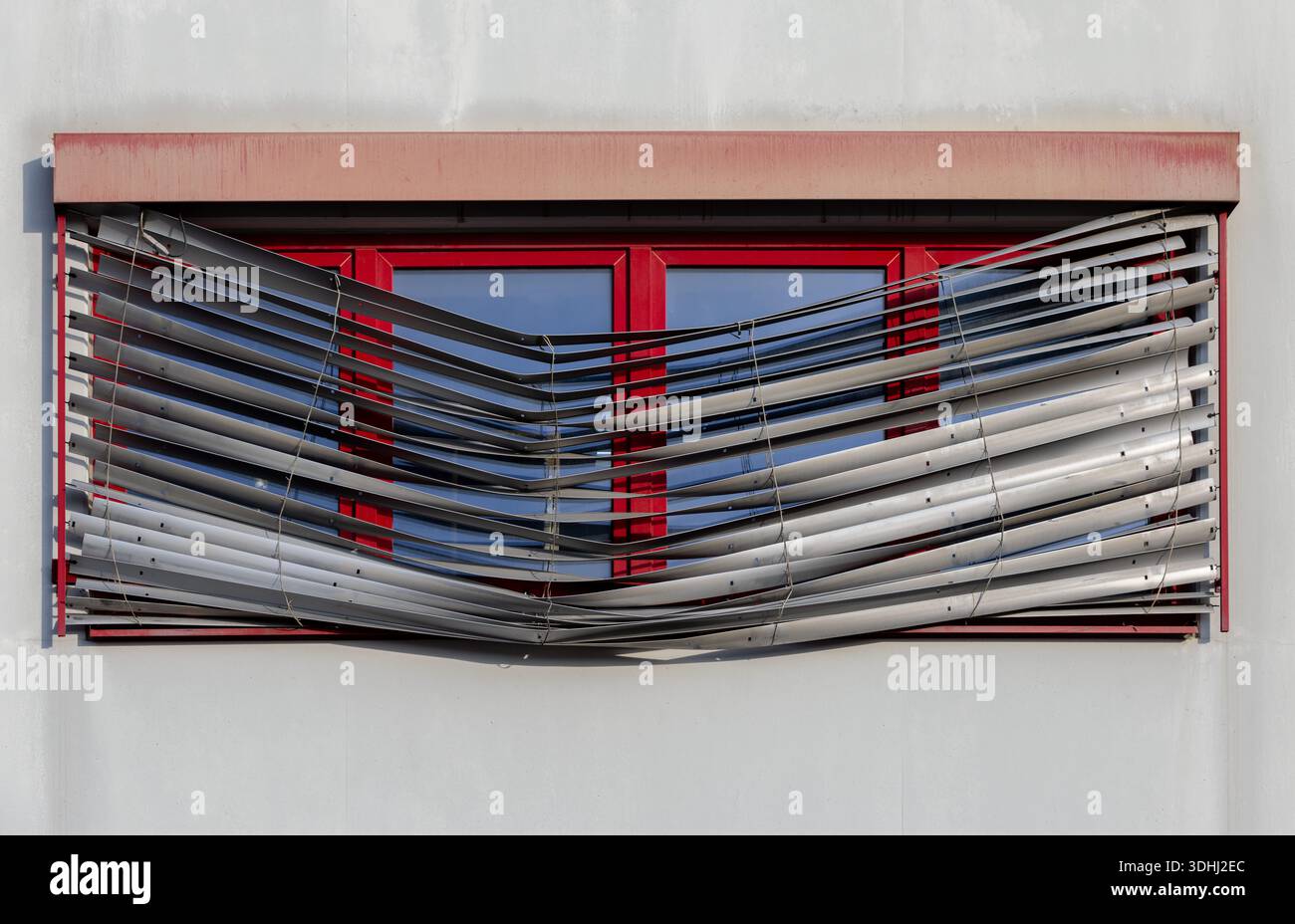 Repairs Needed - Red windows with broken exterior venetian blinds on residential building facade Stock Photo