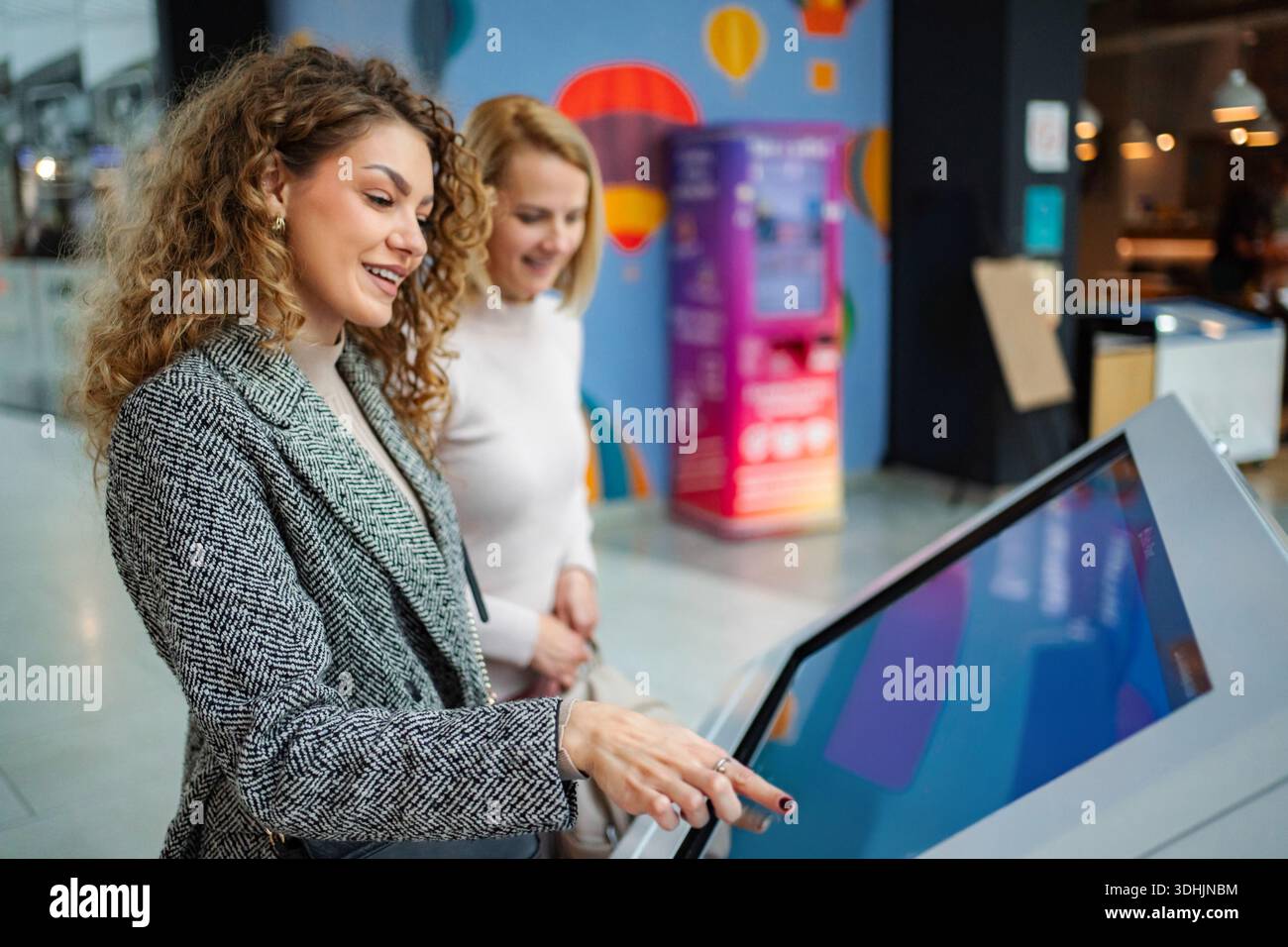 Women friends using interactive digital kiosk touch screen Stock Photo