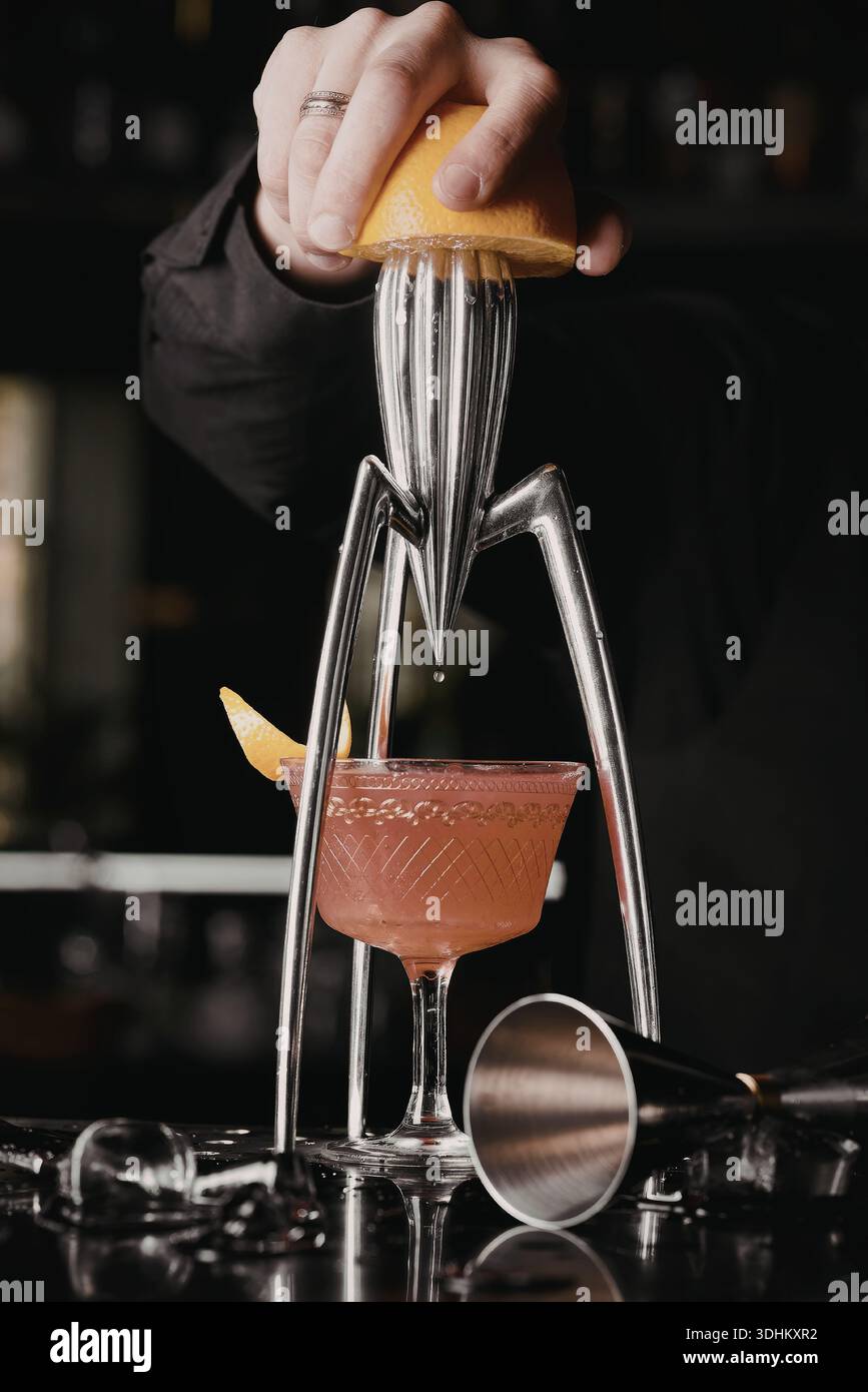 A close-up image of a hand squeezing a lemon into a cocktail shaker ...