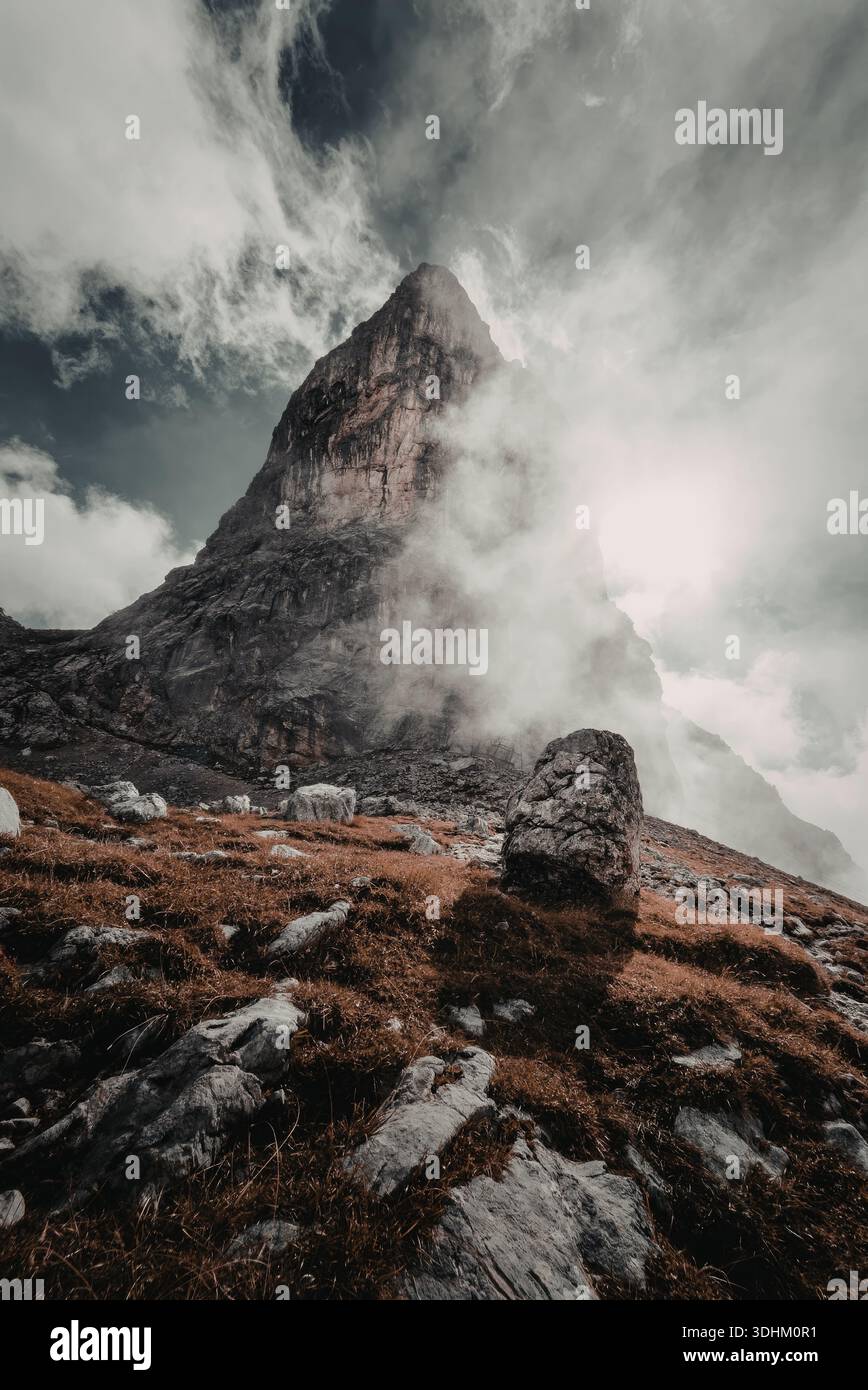 A dramatic mountain peak shrouded in mist and clouds, with rugged ...