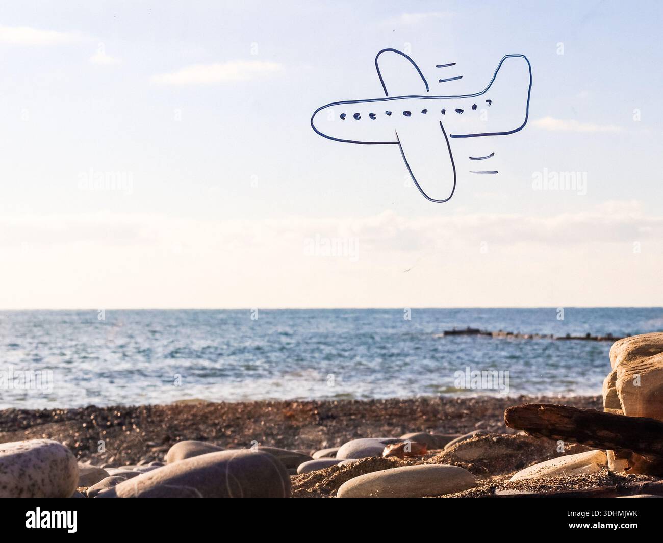 Simple hand-drawn plane with trail in sky above vast ocean horizon and stones on shore Stock Photo