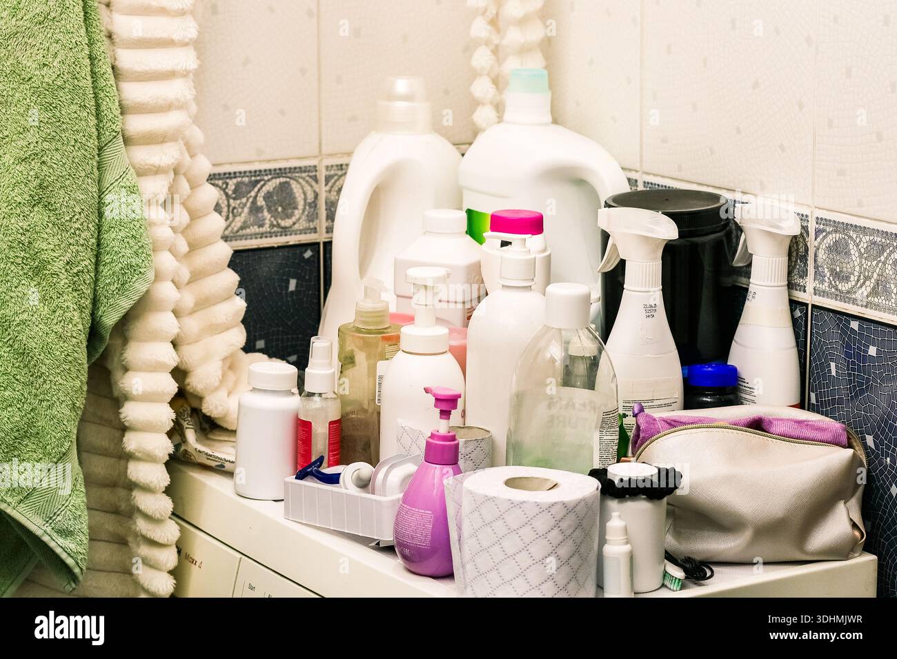 Cluttered bathroom counter with various plastic bottles, sprays, and personal care items next to a green towel Stock Photo