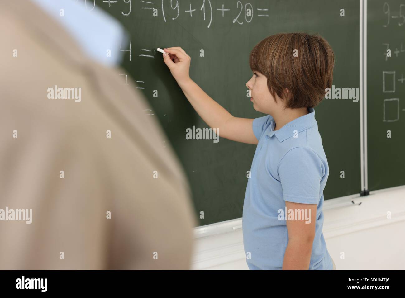 Schoolboy doing math on chalkboard in classroom Stock Photo