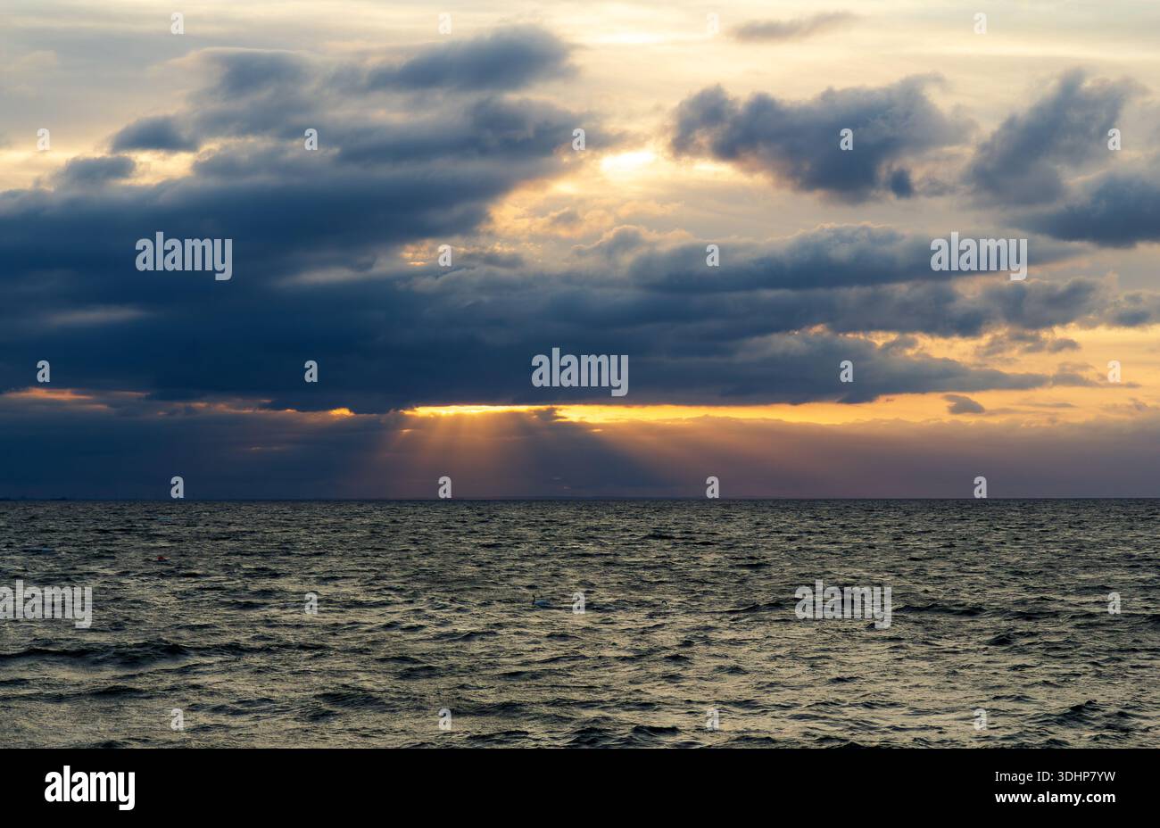 Dramatic seascape with sun rays breaking through dark storm clouds over the ocean Stock Photo