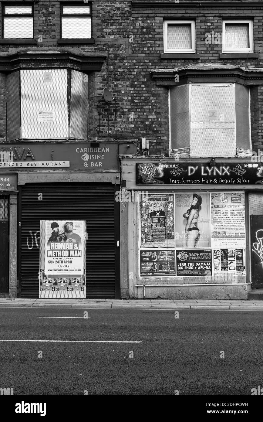 Derelict boarded-up shops with faded signage and graffiti, beneath rundown flats on a worn urban street showing decay, neglect and urban decline. Stock Photo