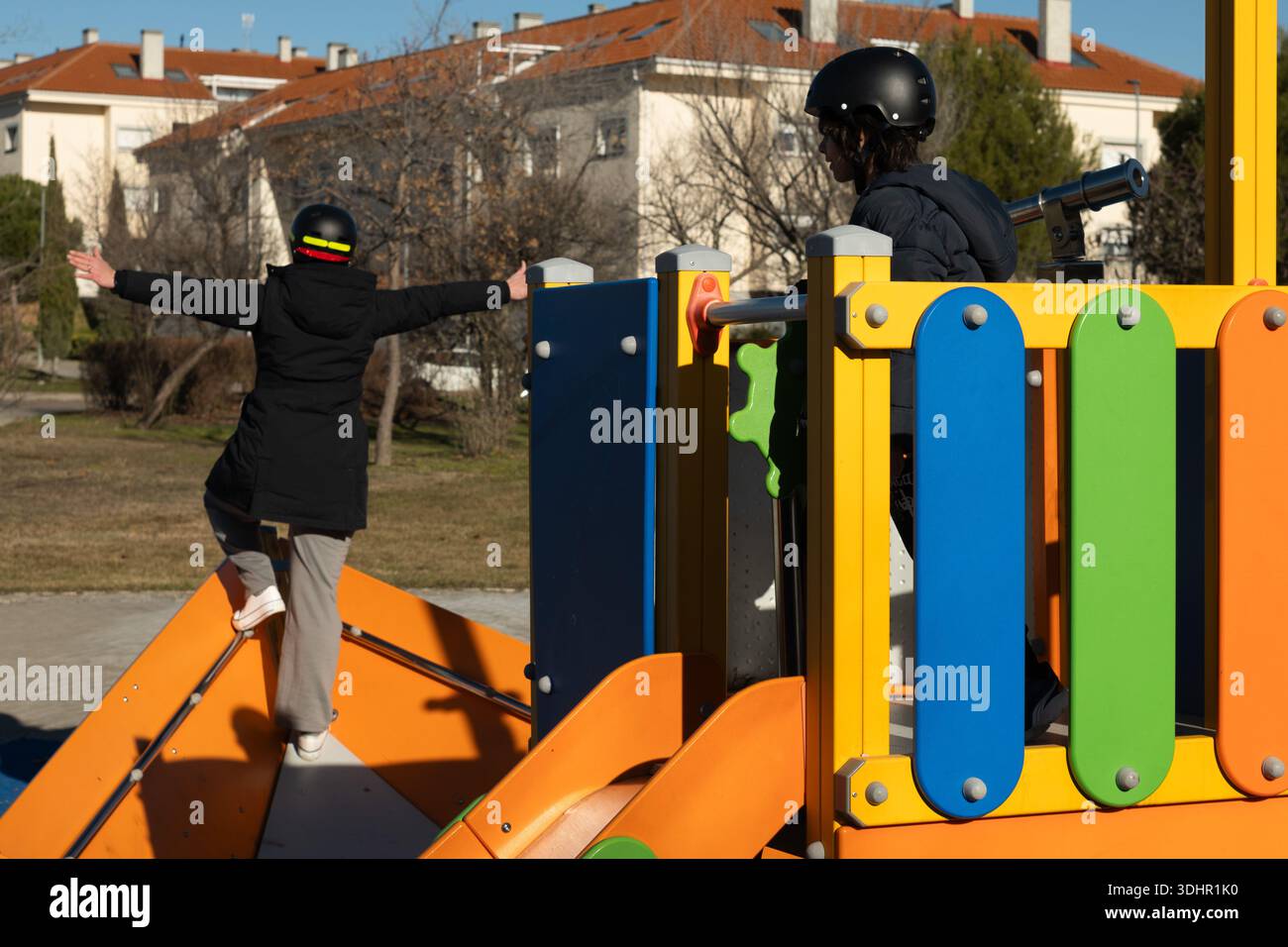 Two children wearing helmets having fun on a colorful playground structure Stock Photo