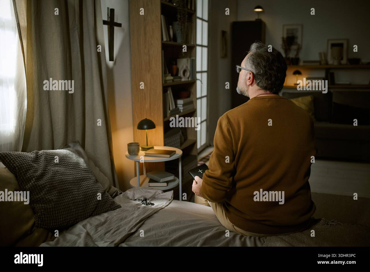 Middle Aged Man Praying Alone While Sitting on Bed at Home Stock Photo