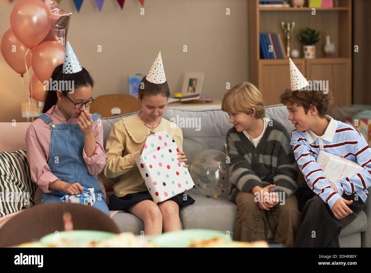Group of children sitting on sofa wearing party hats, Caucasian and ...
