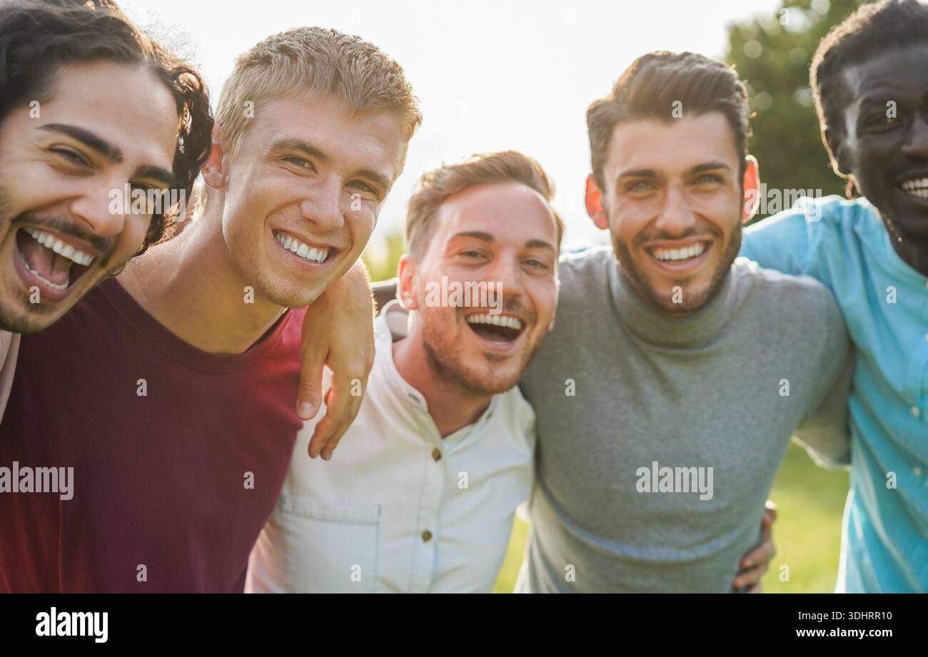 Happy male friends having fun together outdoor - Group of multiracial men hugging each other at city park - Friendship and lifestyle concept Stock Photo
