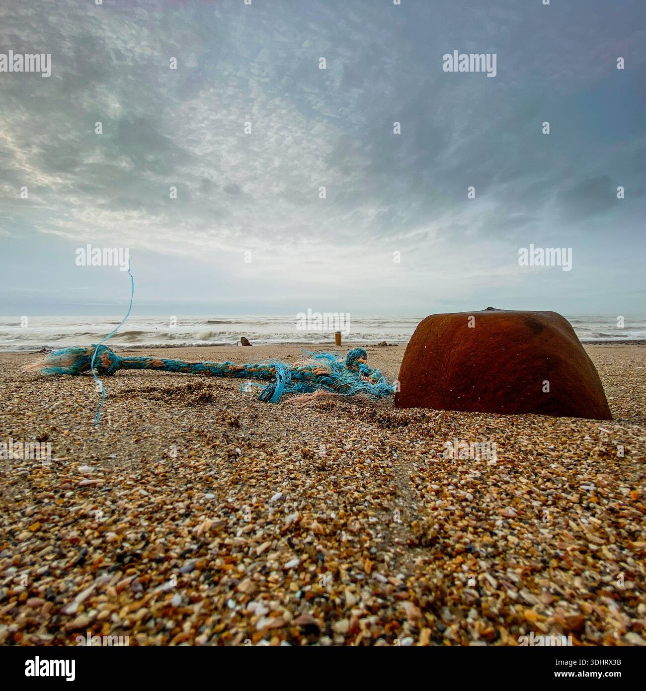 Low view of a pebbled beach with blue rope and a wodden groyne under a brooding sky on the British coast. - Smartphone Captured Stock Image