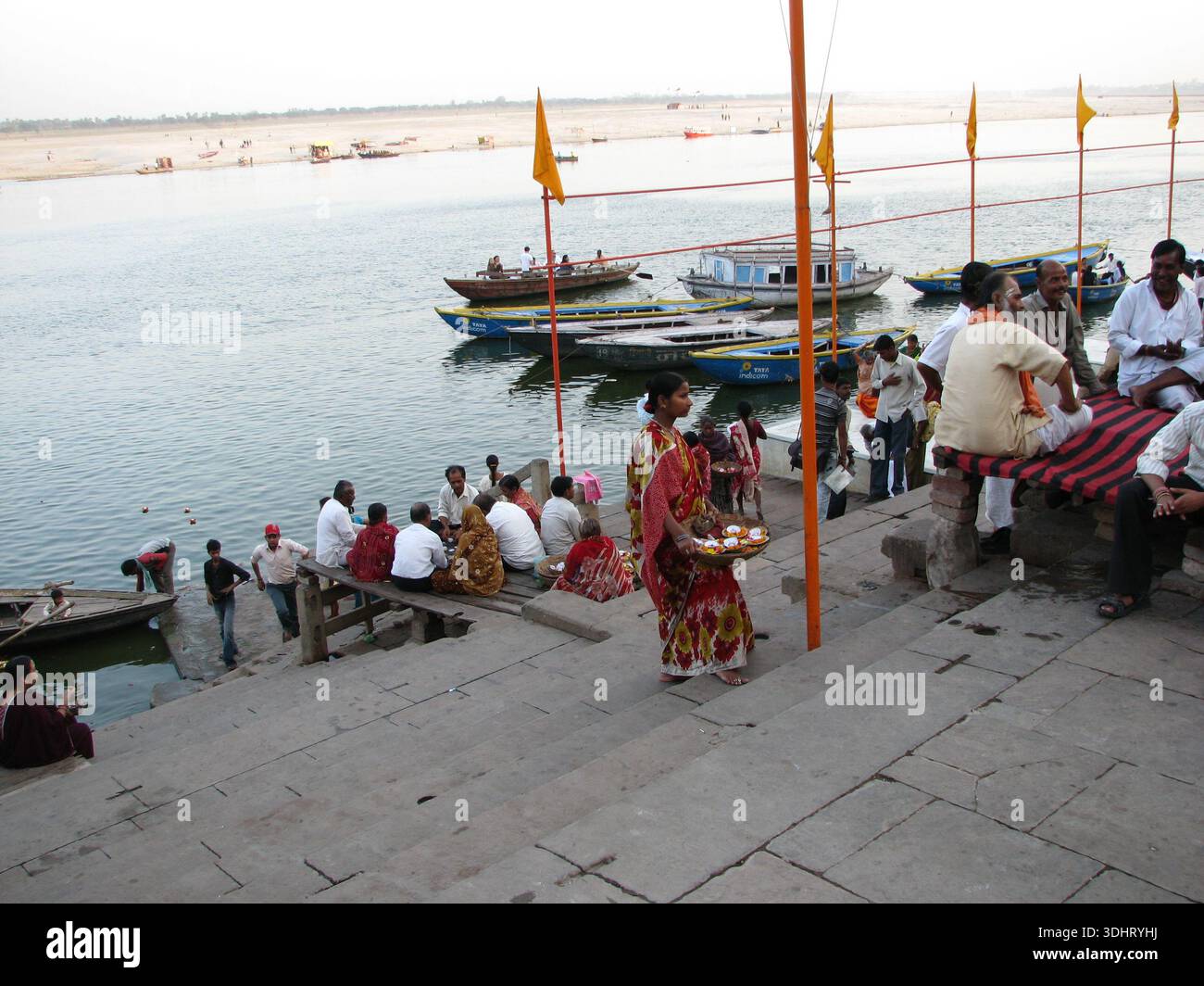 People sit and walk on riverside steps beside boats on the Ganges River ...