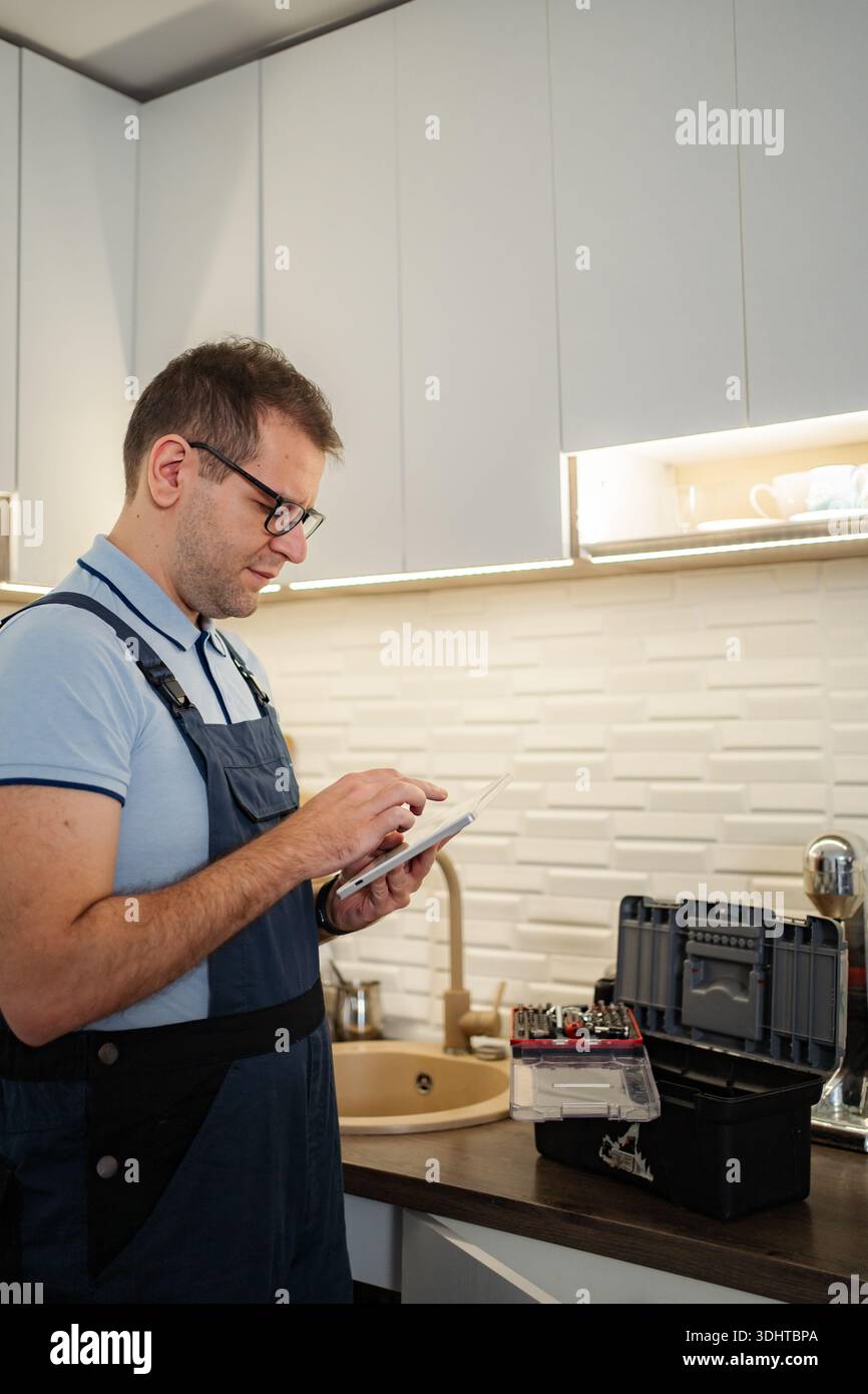 Handyman using tablet near toolbox in modern kitchen Stock Photo