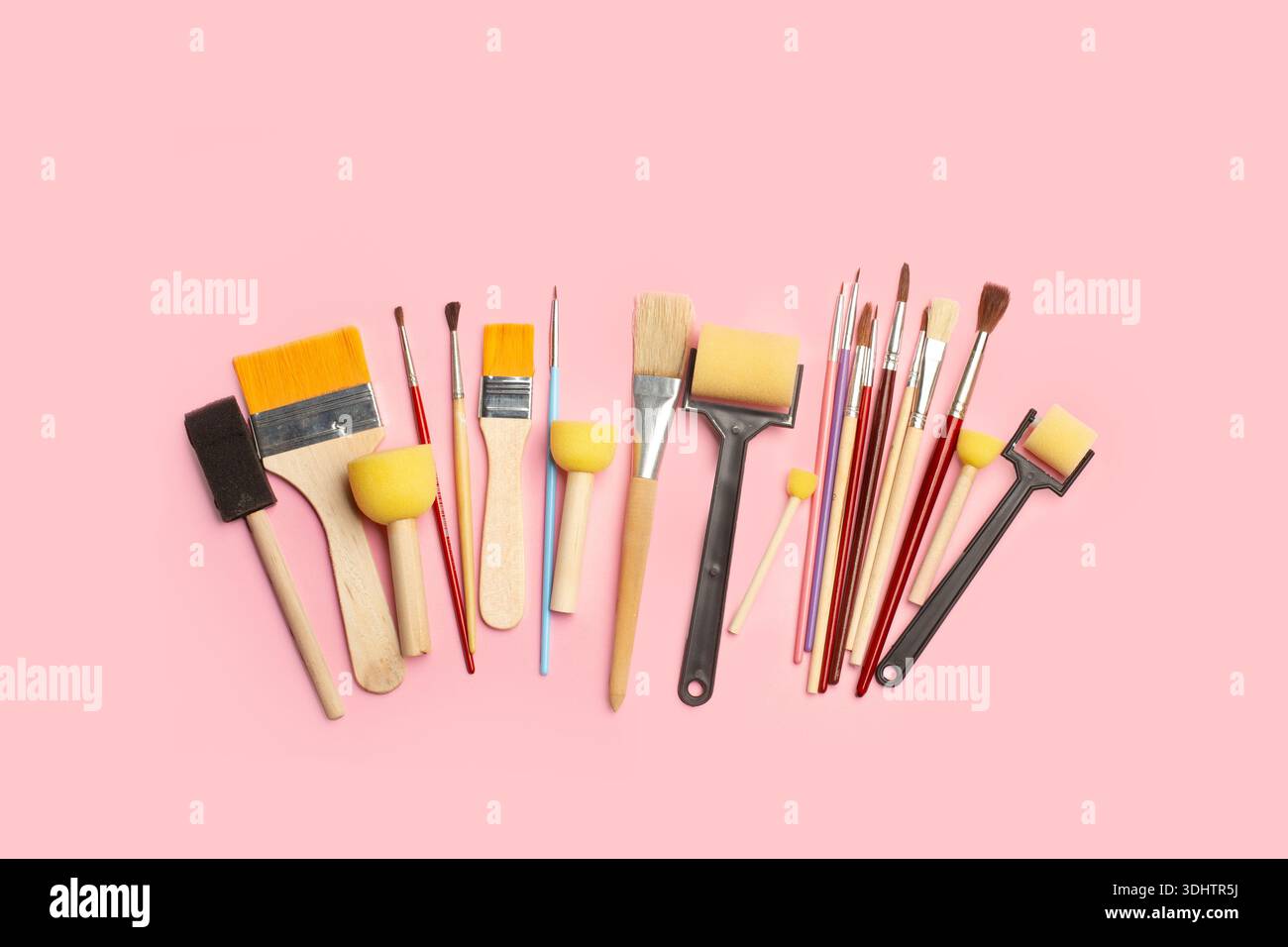 Colored artistic paintbrushes, roller brushes and sponge foam brushes on a pink background with copy space Stock Photo