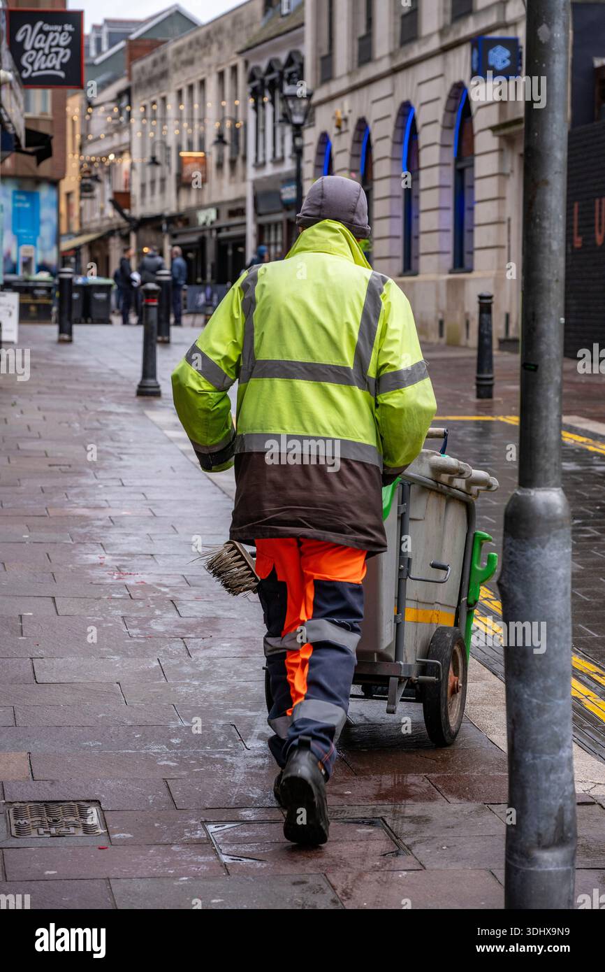 Street cleaning operative in high visibility clothing taking a break  leaning against bench seat Stock Photo