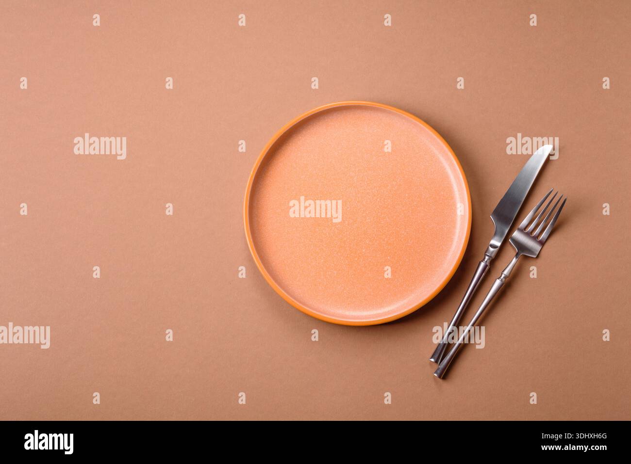 An empty round ceramic plate, knife, and fork as a dining table setting. An empty plate as a backdrop for your design Stock Photo