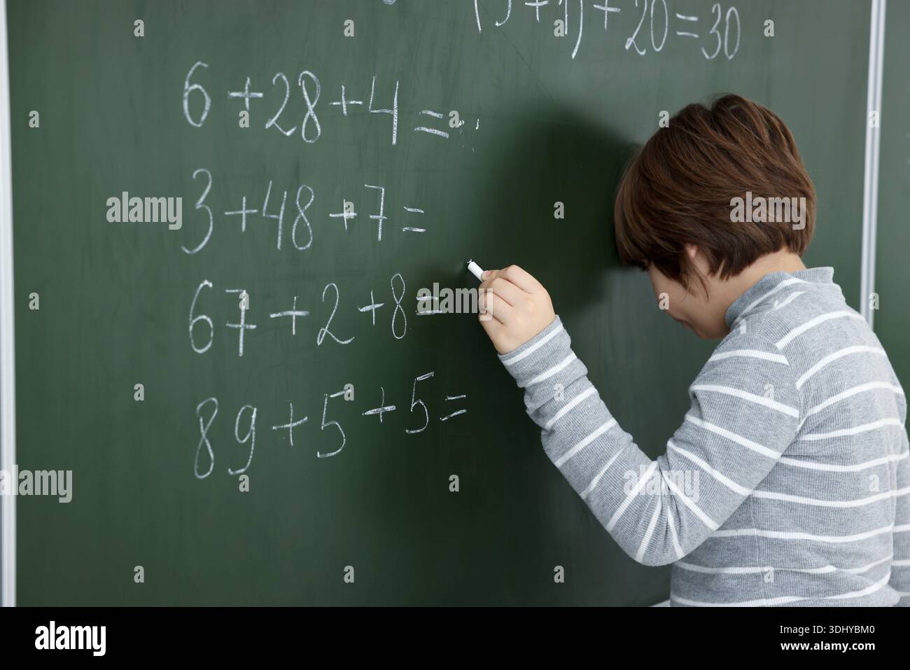 Schoolboy doing math on chalkboard in classroom Stock Photo