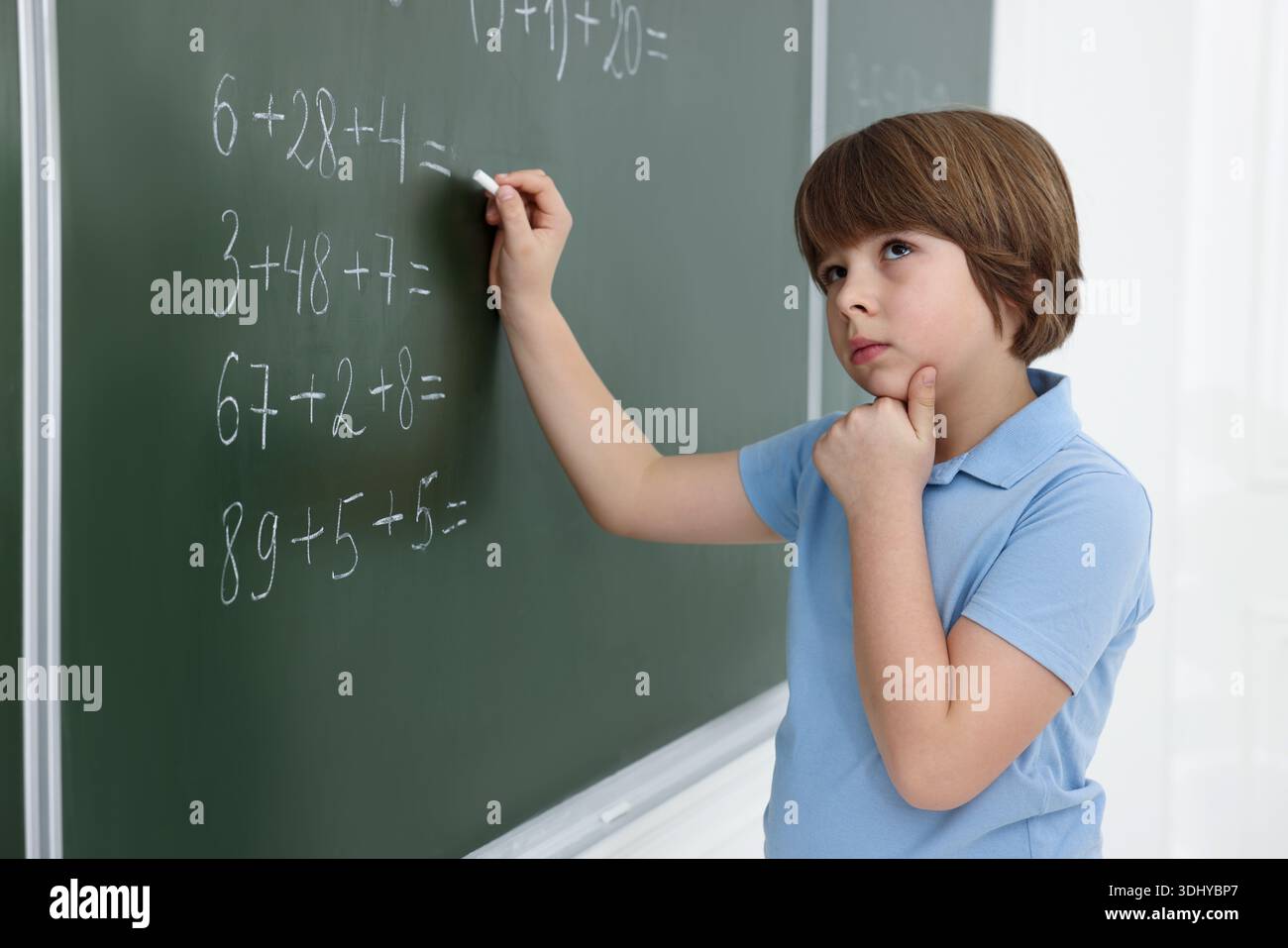 Schoolboy doing math on chalkboard in classroom Stock Photo
