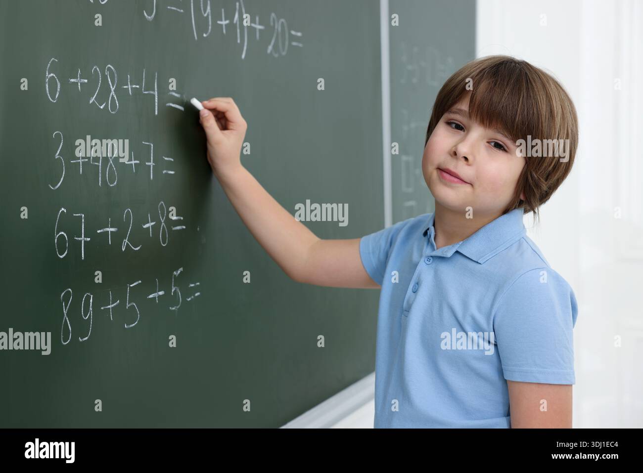 Schoolboy doing math on chalkboard in classroom Stock Photo