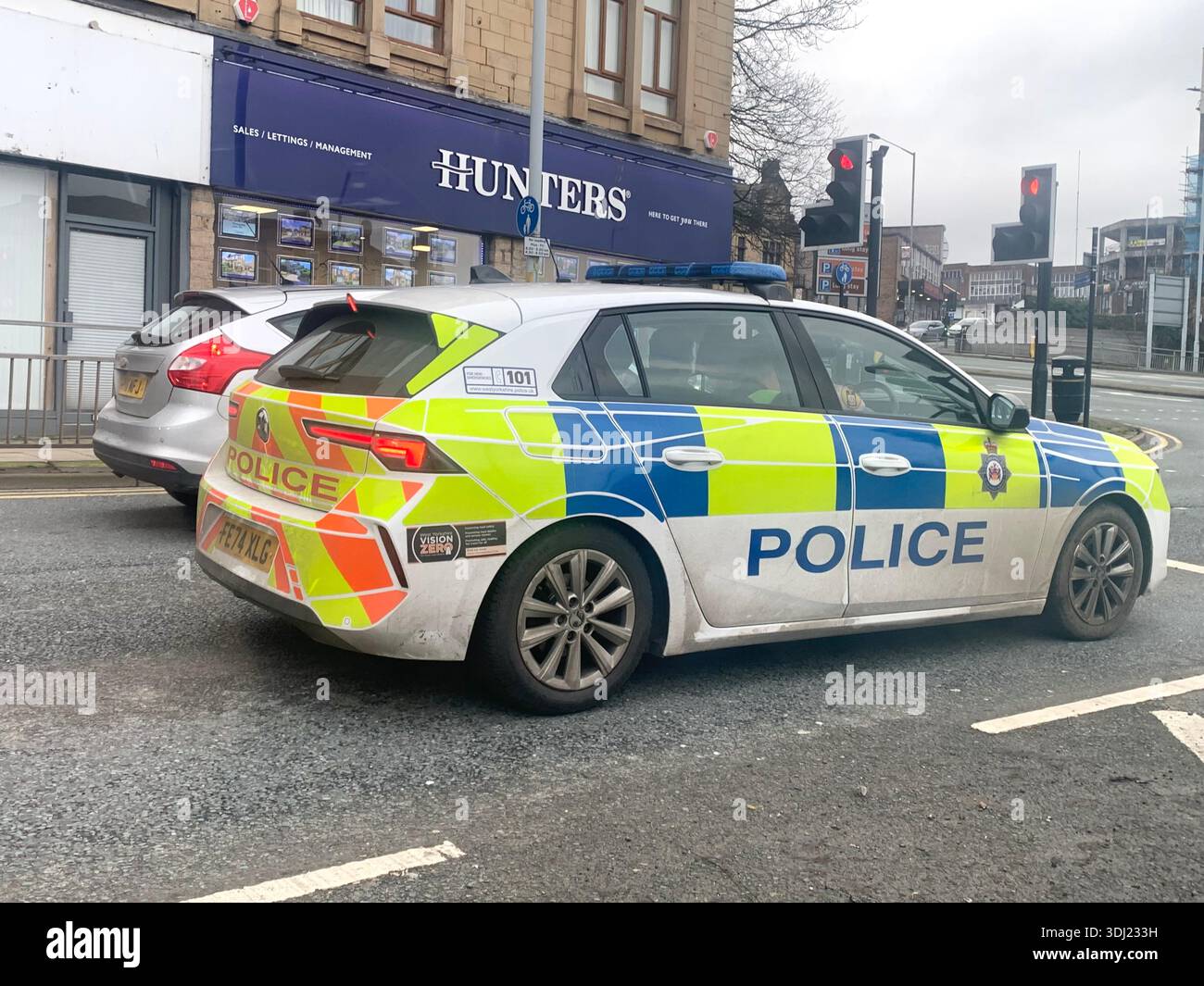 Marked British Police car parked on a city street near traffic lights with commercial buildings in the foreground illustrating urban law enforcement - Smartphone Captured Stock Image