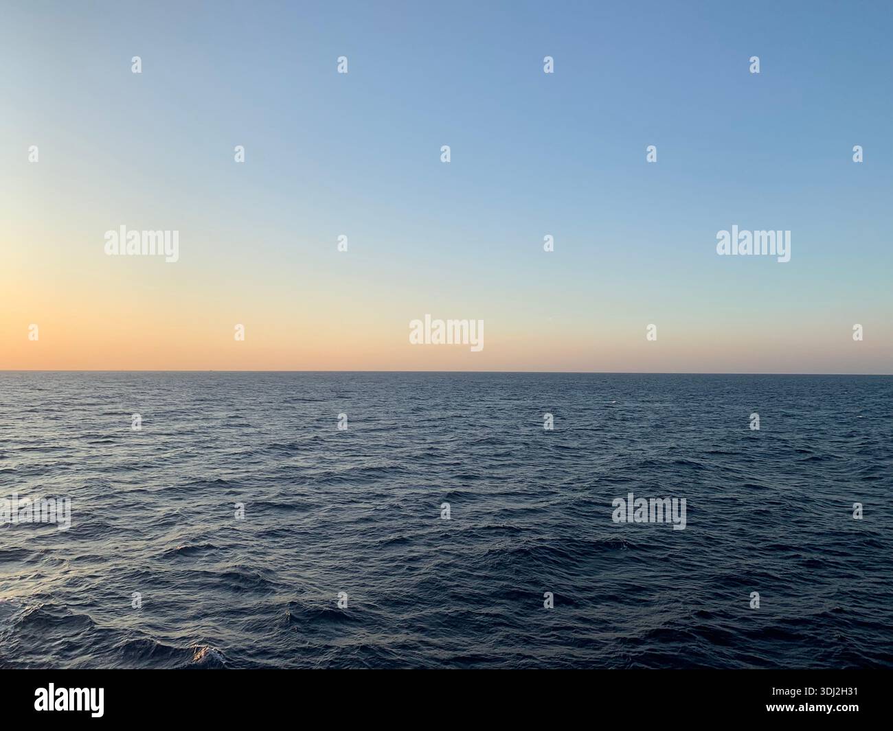 Calm open sea with gentle waves under a clear sky during golden hour, featuring a peaceful ocean horizon and soft gradient colors at sunset. - Smartphone Captured Stock Image