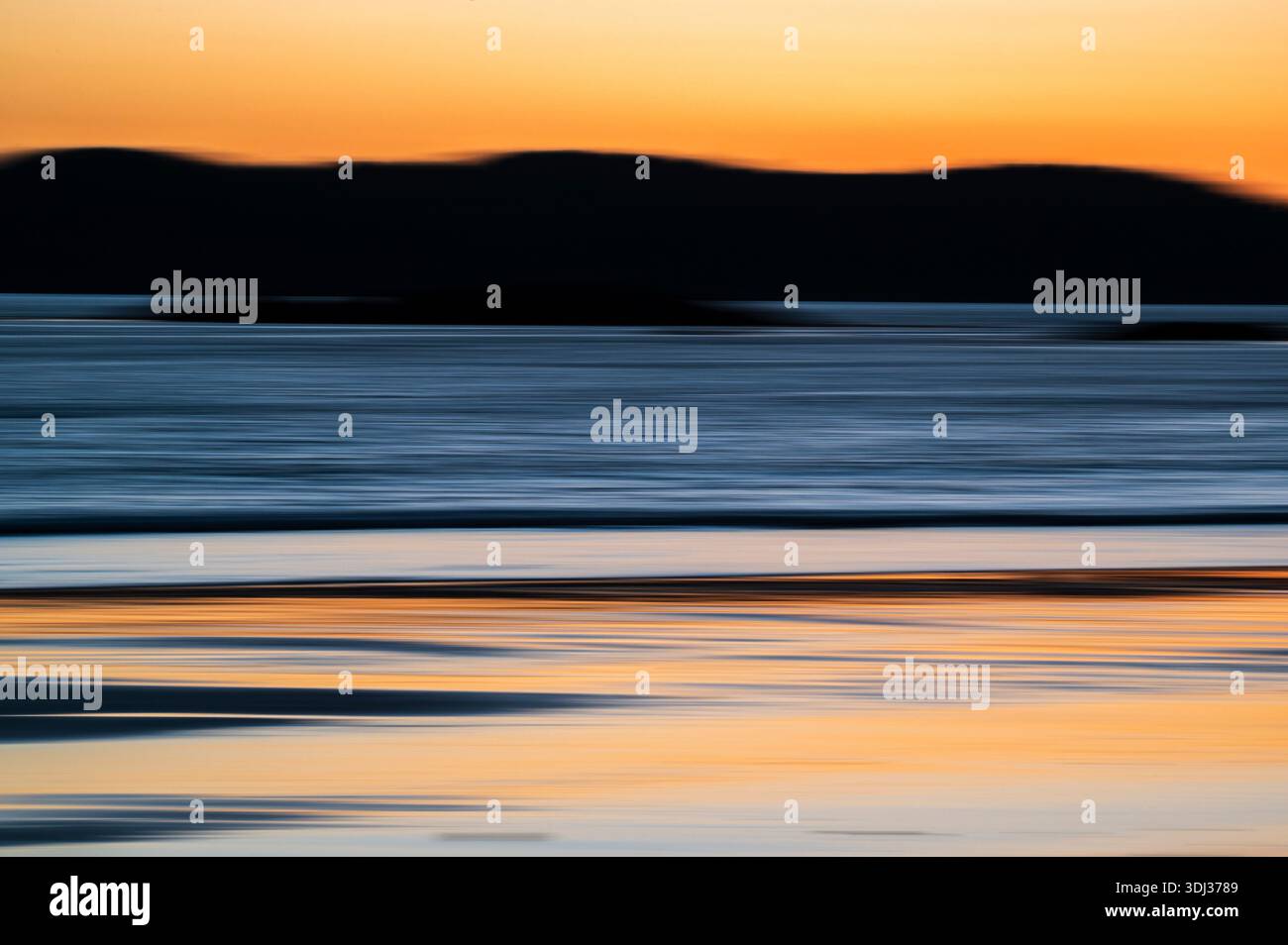 A serene seascape at sunset features horizontal streaks of warm orange, deep blue, and soft gray, creating a painterly, abstract effect. The blurred m Stock Photo