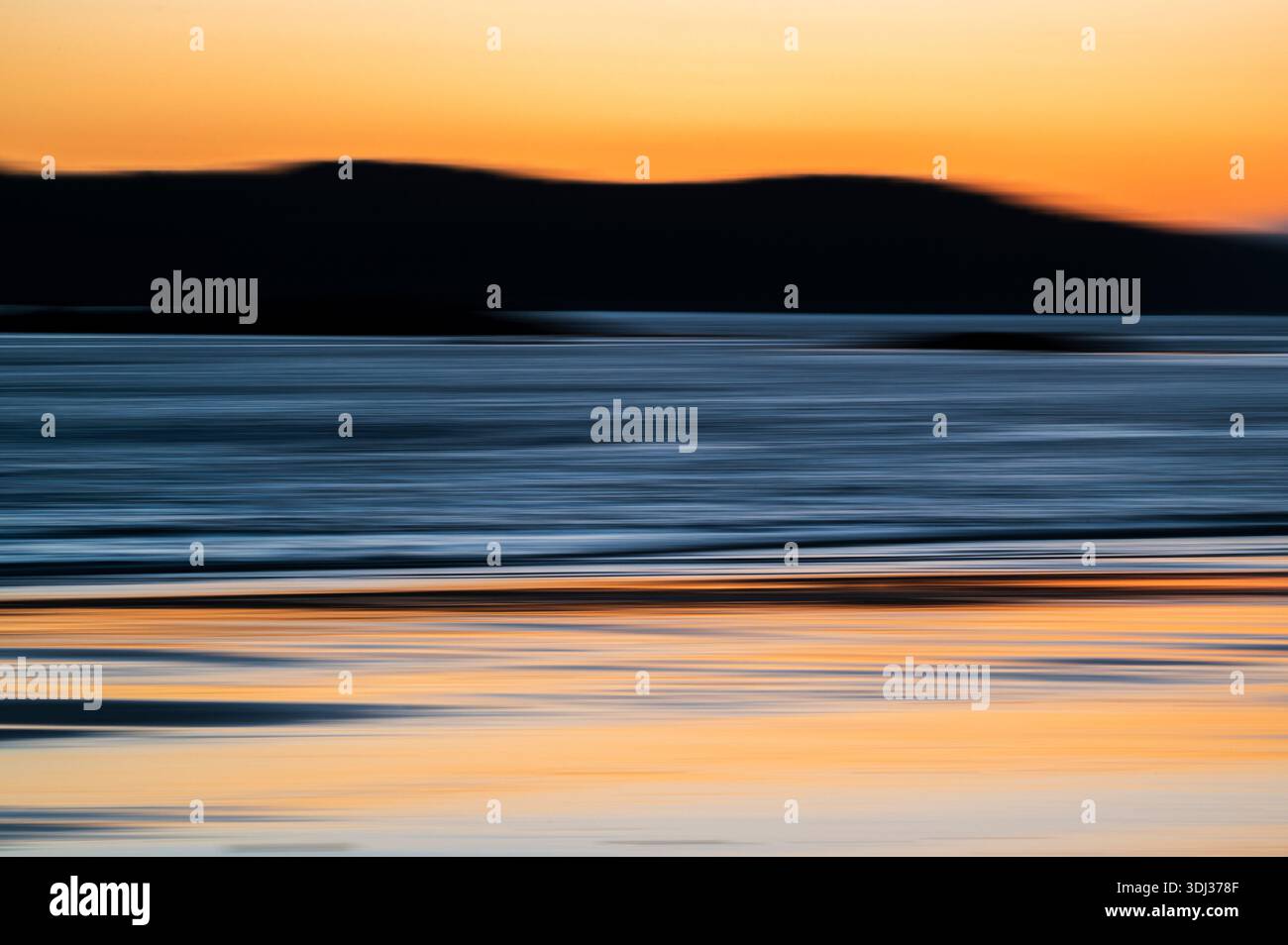 A serene seascape at sunset features horizontal streaks of warm orange, deep blue, and soft gray, creating a painterly, abstract effect. The blurred m Stock Photo