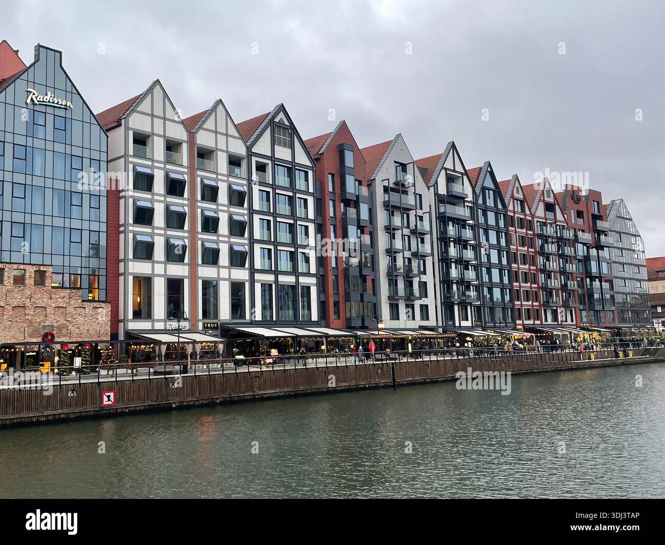 Modern waterfront buildings and restaurants along the Motława River in the Old Town of Gdańsk on an overcast day. - Smartphone Captured Stock Image