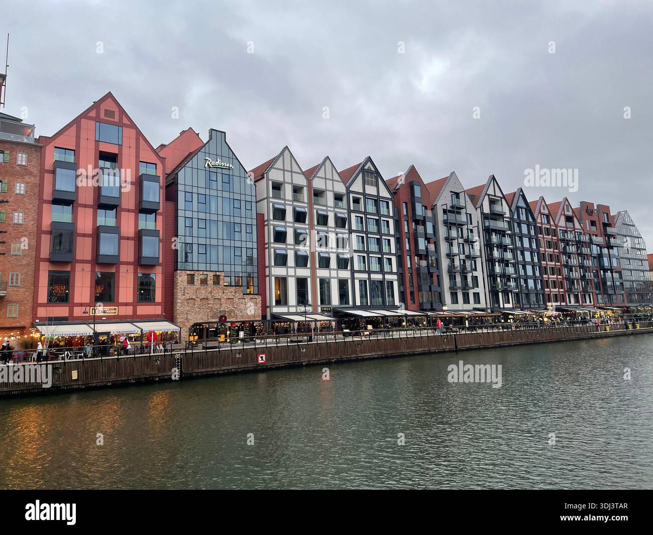 Modern waterfront buildings and restaurants along the Motława River in the Old Town of Gdańsk on an overcast day. - Smartphone Captured Stock Image