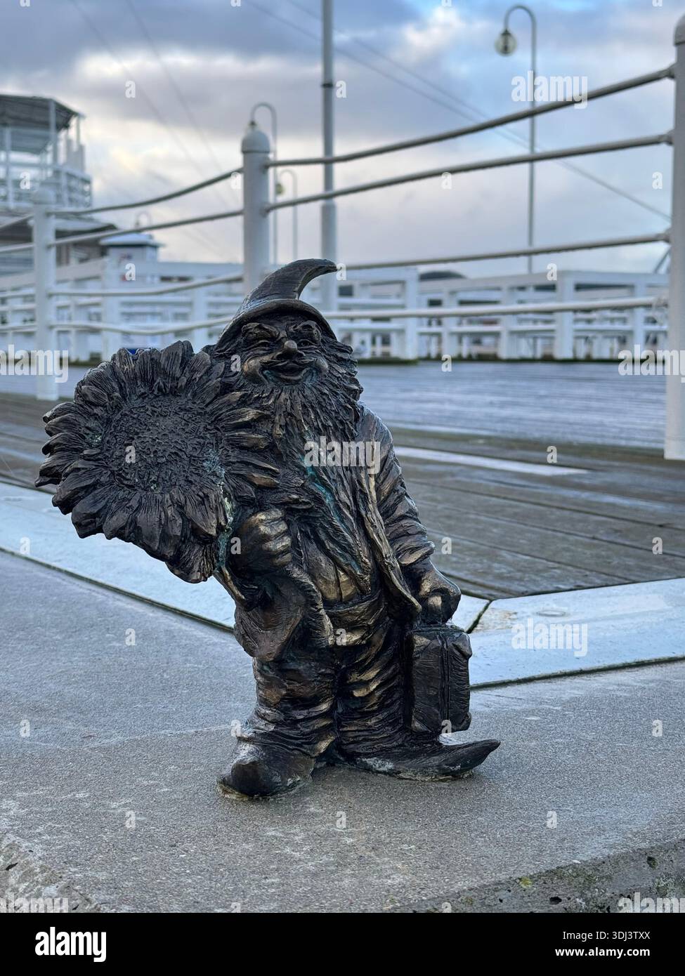 Small bronze dwarf sculpture standing on the pier near the waterfront of Sopot on a cloudy day. - Smartphone Captured Stock Image