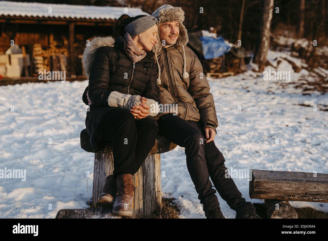 Happy couple sitting on log in snow Stock Photo