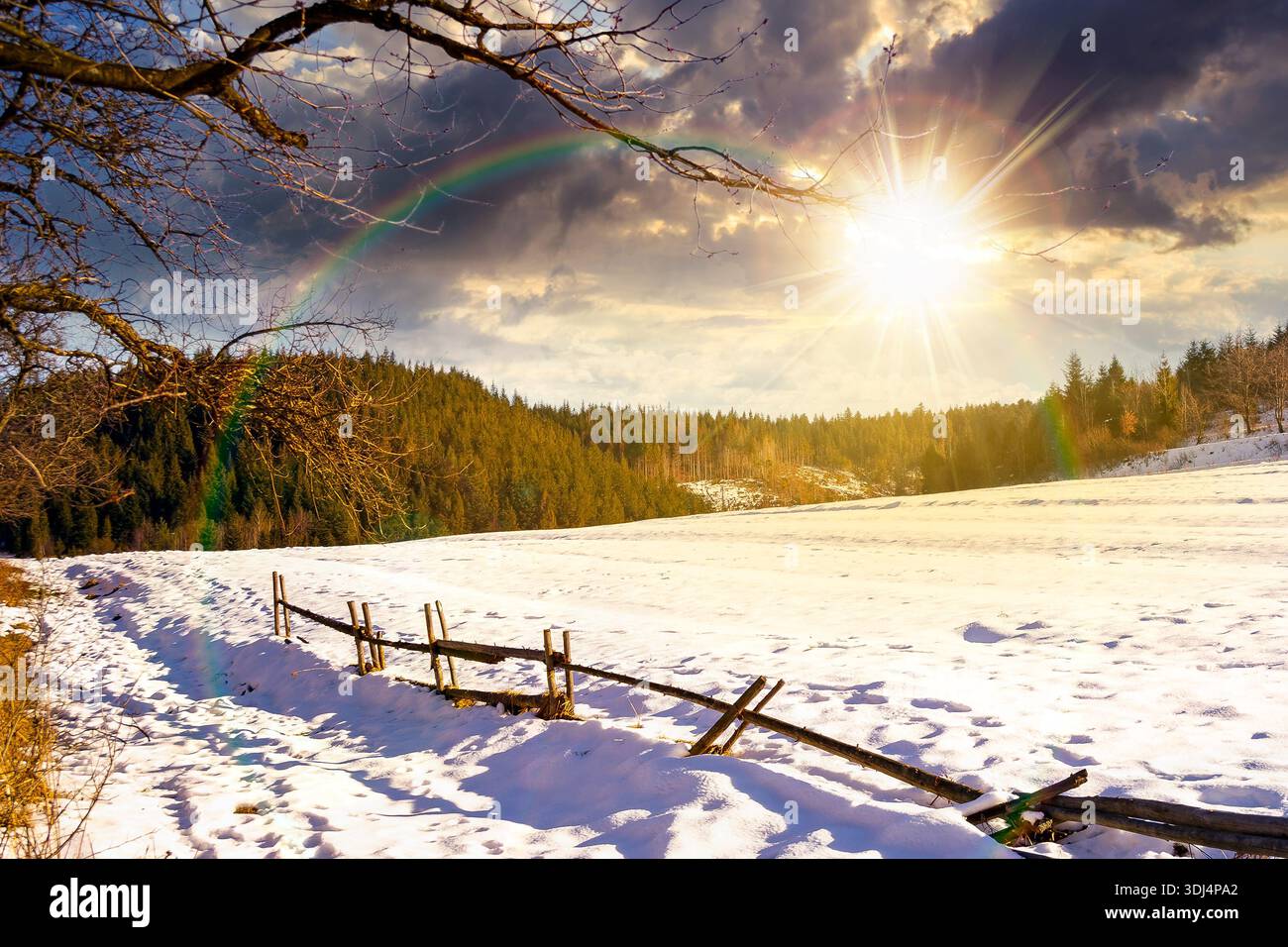 rustic wooden fence through snow covered hill at sunset. beautiful view in winter mountains in evening light. alpine rural landscape near forest. lead Stock Photo