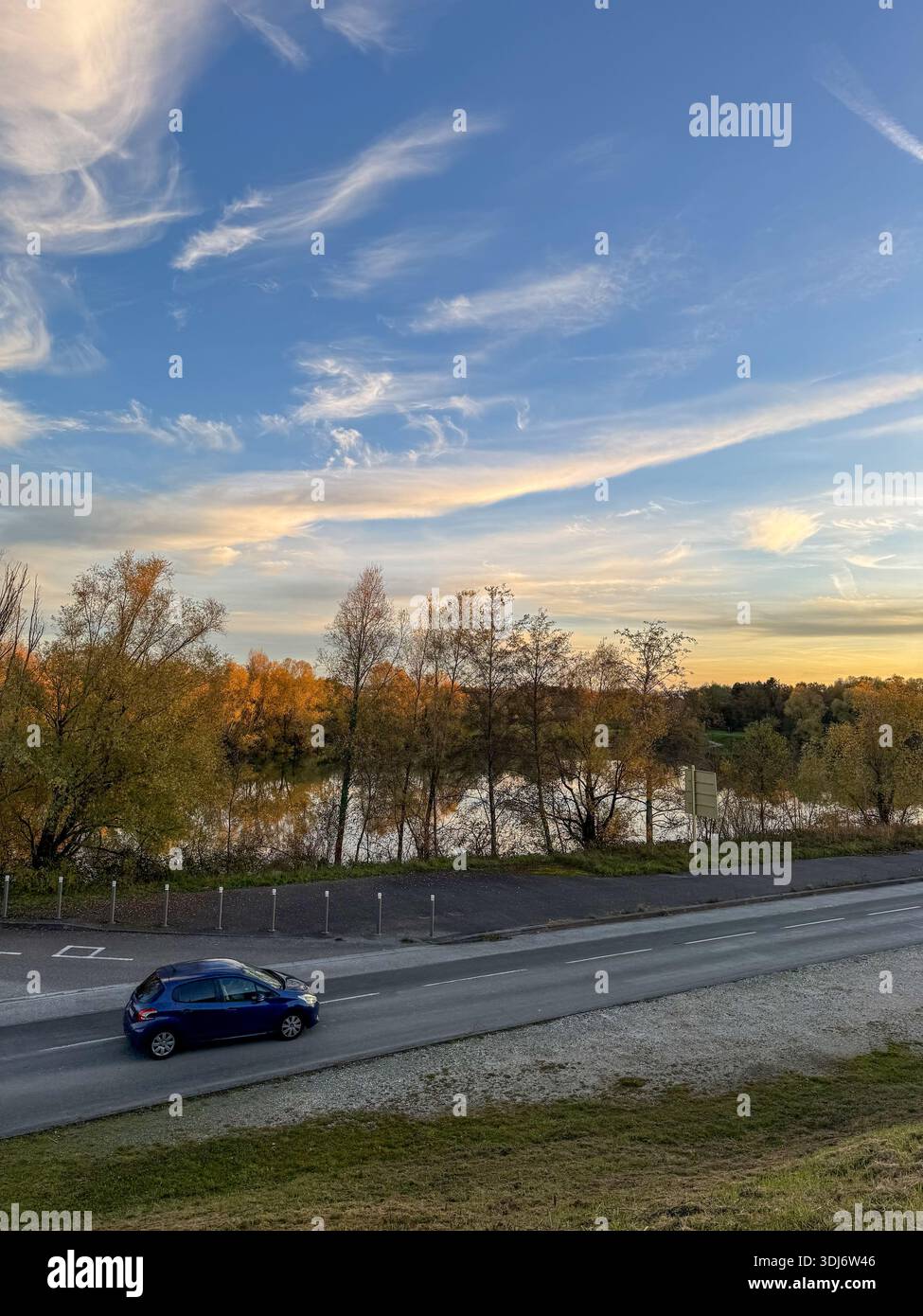 autumn landscape along a quiet road near the doubs river, with golden fall foliage reflected in calm water under a soft evening sky. - Smartphone Captured Stock Image