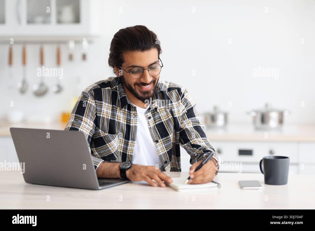 Positive arab guy looking for job online, kitchen interior Stock Photo