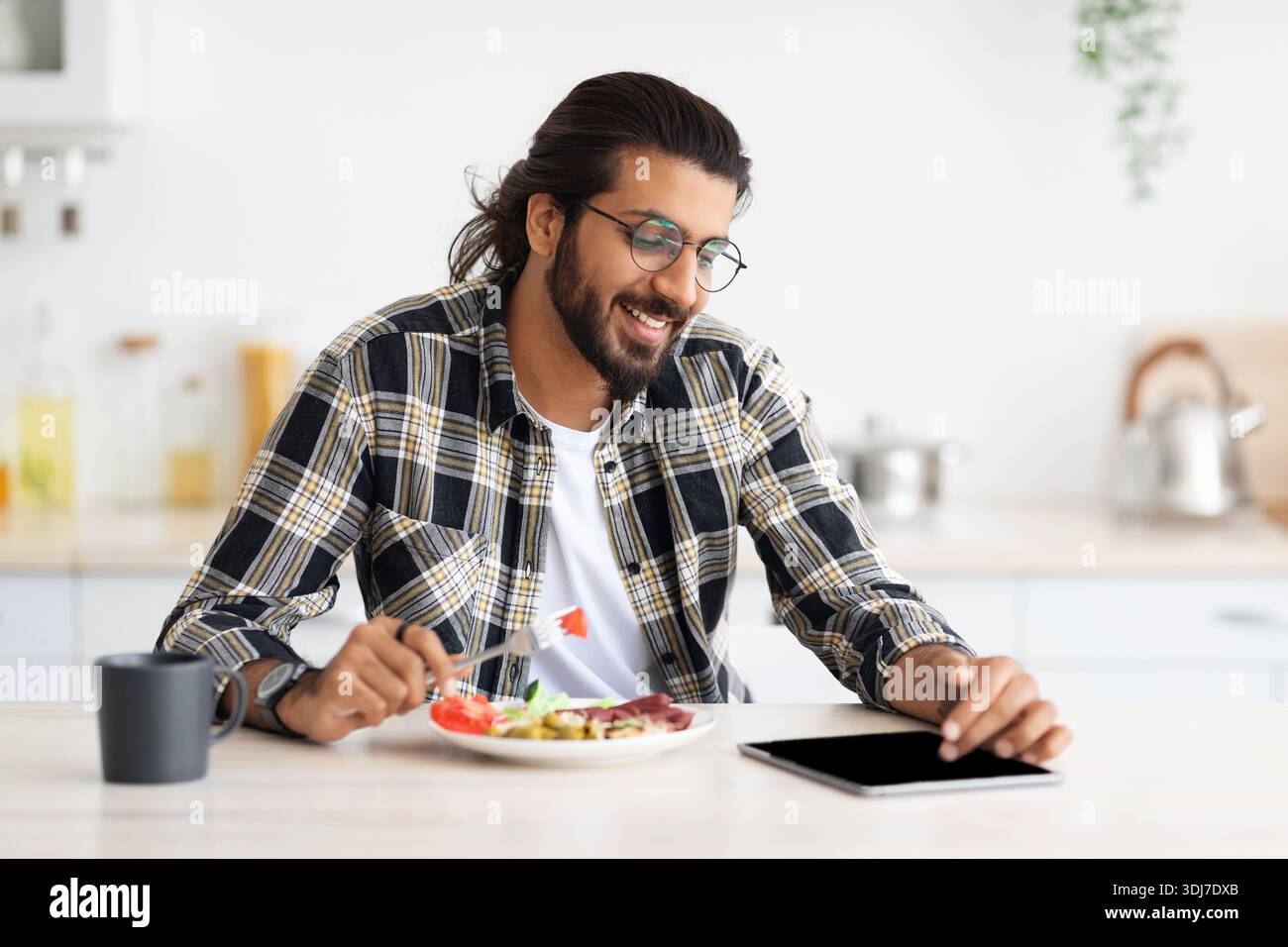 Happy indian guy having lunch and using digital tablet Stock Photo