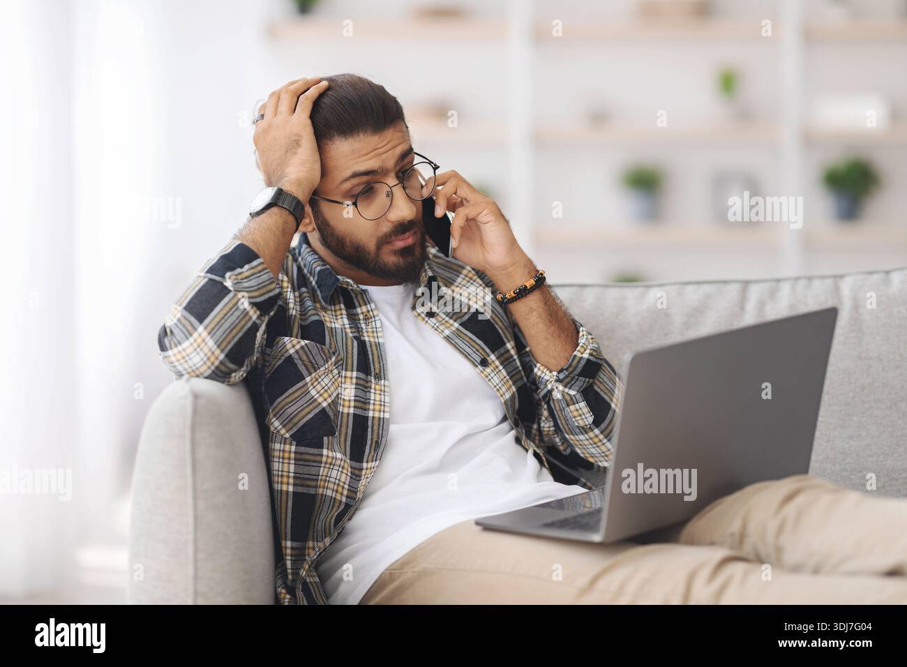 Stressful indian guy with laptop having phone conversation Stock Photo