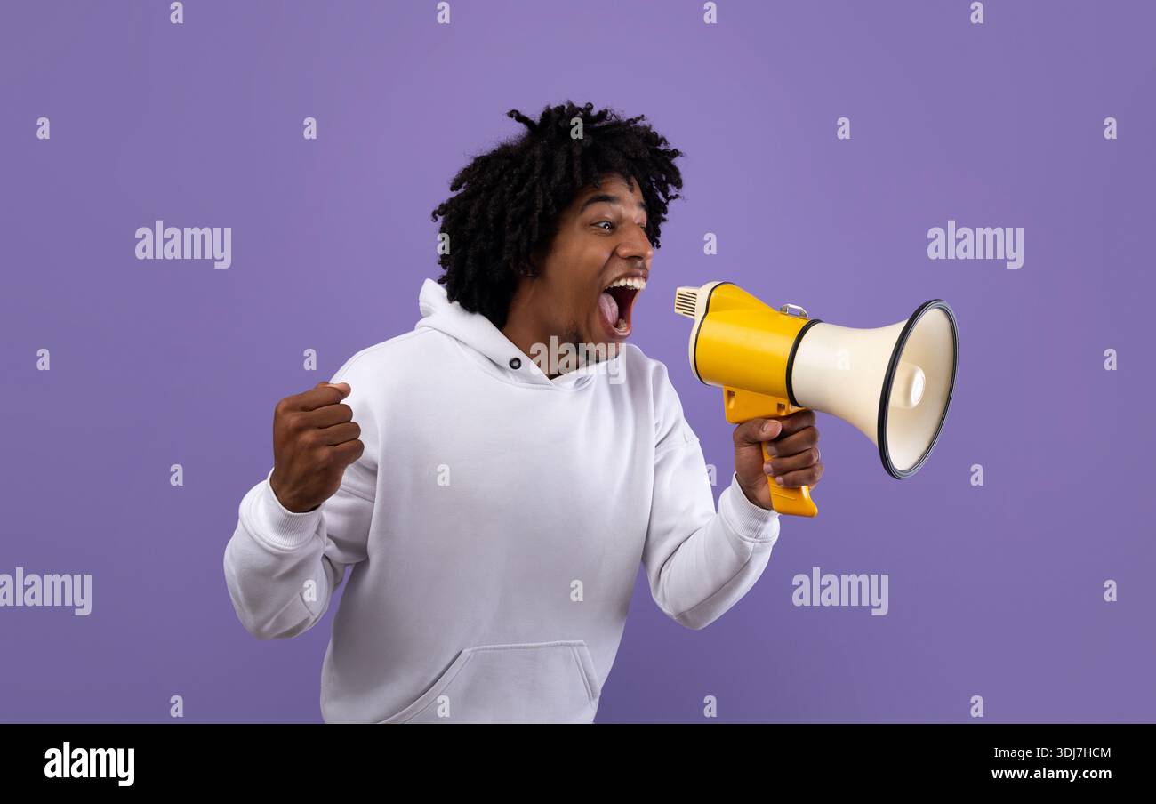 Emotional black adolescent shouting into megaphone, making announcement over violet studio background Stock Photo