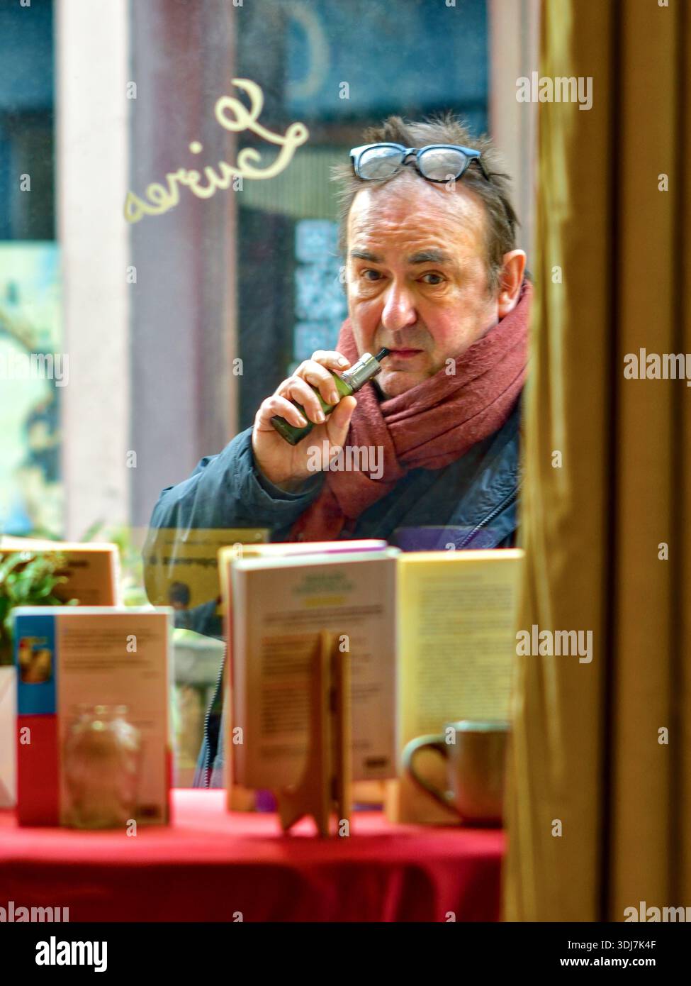 Man vaping and with glasses on forehead looking into a bookshop window from outside - Loches, Indre-et-Loire (37), France. Stock Photo