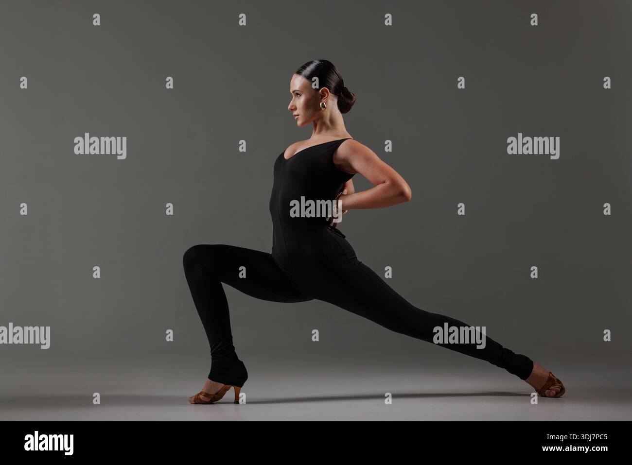 Confident female dancer in black bodysuit holding dramatic lunge pose, showcasing balance, strength, and expression. Stock Photo