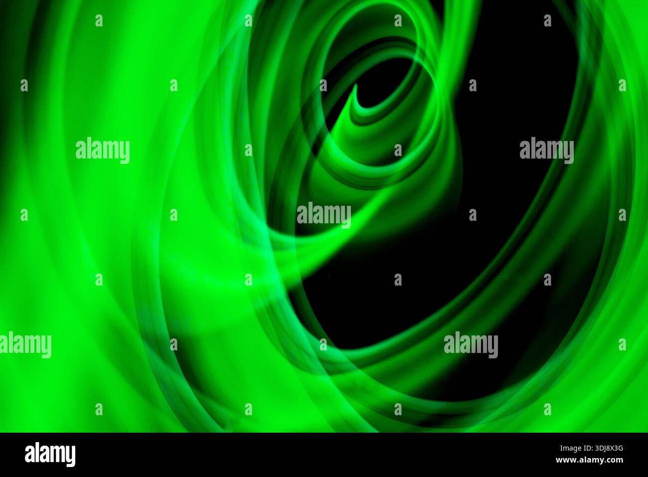 Circular green energy vortex forming hypnotic abstract motion with luminous glow on dark background. Stock Photo