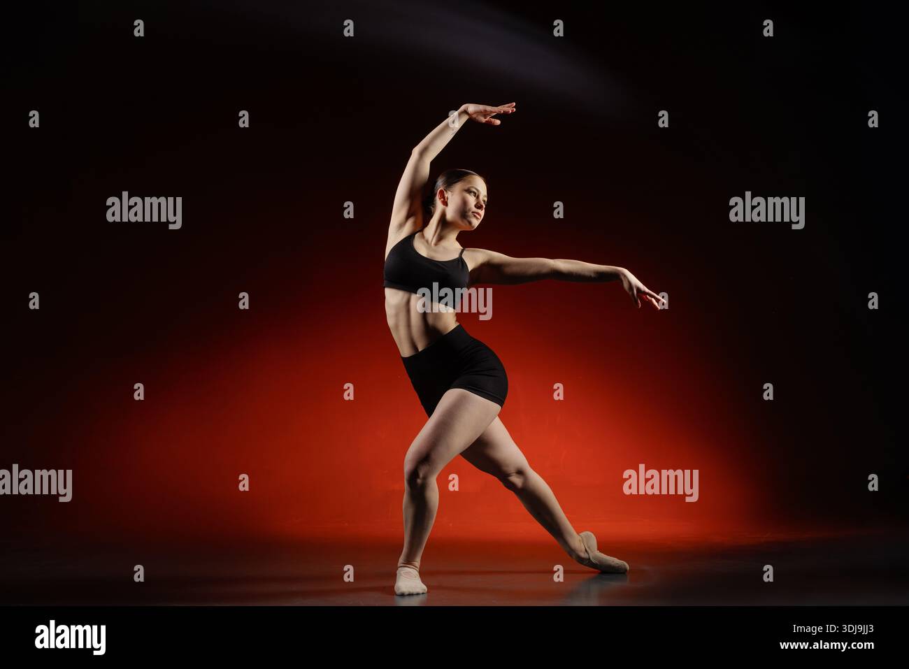 Full length female dancer doing side stretch pose in studio with red Stock Photo