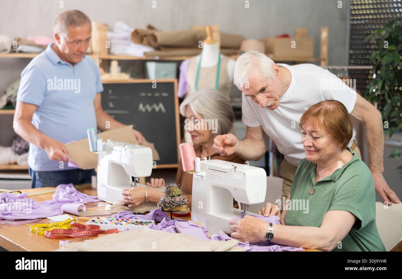 Some people communicate and discuss pattern, while others sew using sewing machine at lesson Stock Photo